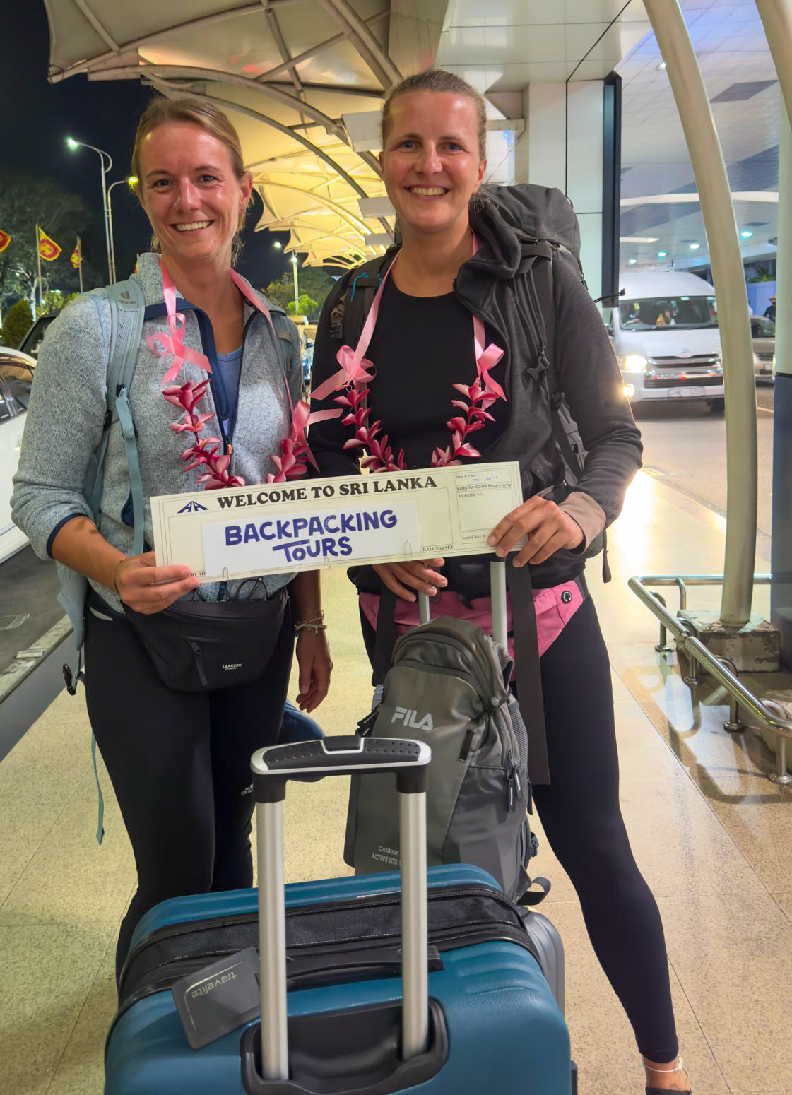 Two happy women with leis and luggage arrive in Sri Lanka for a backpacking tour.