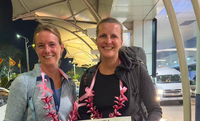 Two happy women with leis and luggage arrive in Sri Lanka for a backpacking tour.