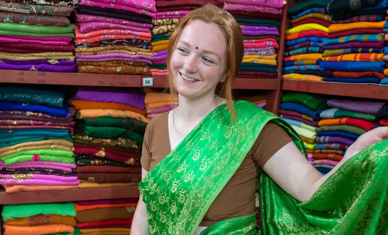 Smiling woman in a green sari among colorful fabric stacks in a Sri Lankan shop.