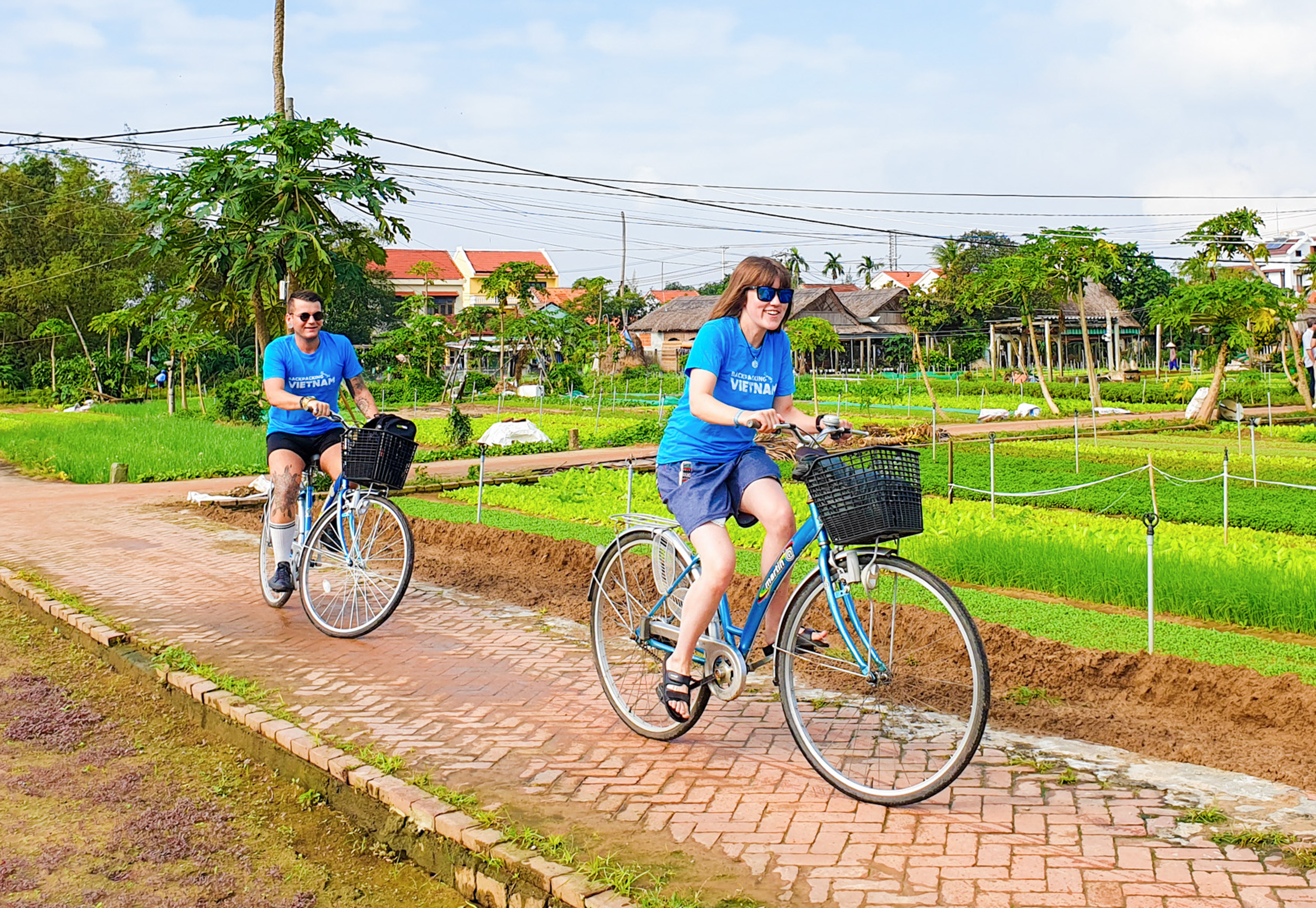 Two tourists in blue shirts happily cycling through vibrant green fields in Vietnam.