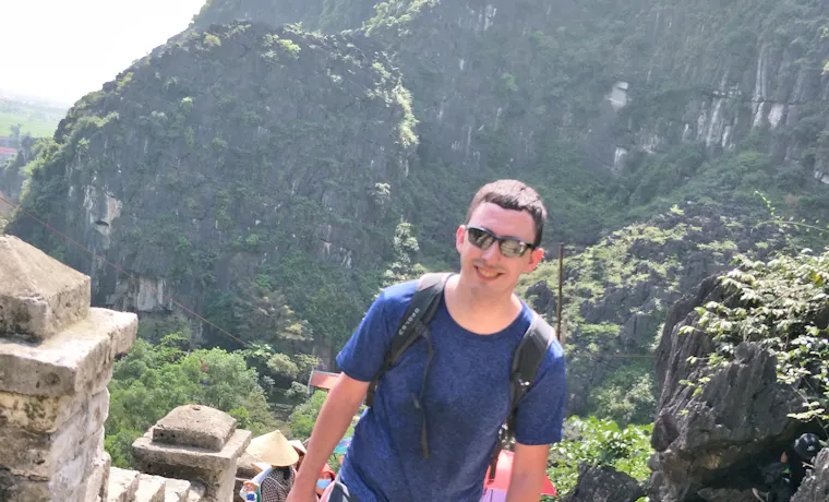 A smiling man hikes up ancient stone steps in Vietnam's scenic karst mountains.