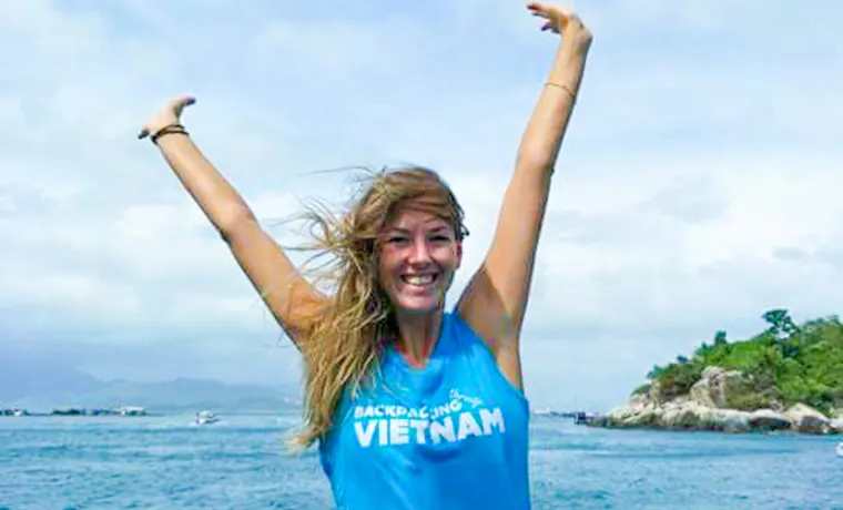 Smiling woman in a 'Backpacking Vietnam' shirt with arms raised on a boat.