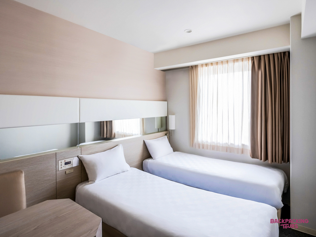 A bright and minimalist twin room in a modern Osaka hotel, featuring two beds and a window.
