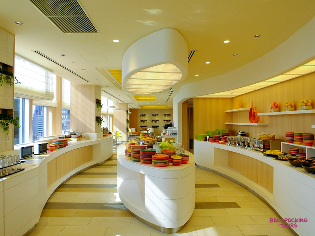 A bright and modern hotel breakfast buffet in Osaka with various food options and colorful plates.