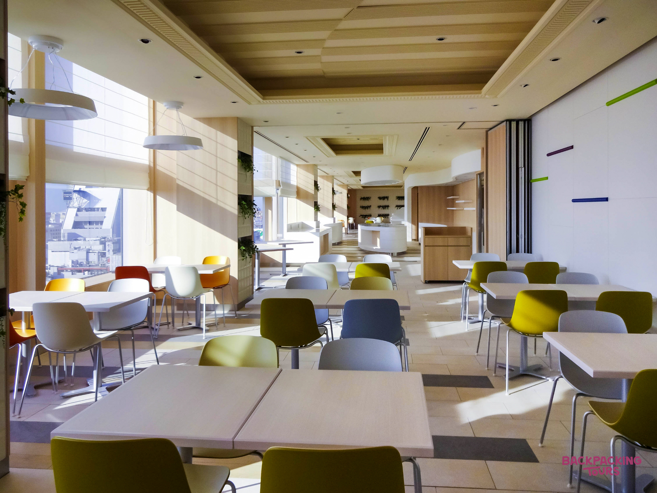 Bright and modern hotel dining room in Osaka, featuring colorful chairs and large sunny windows.