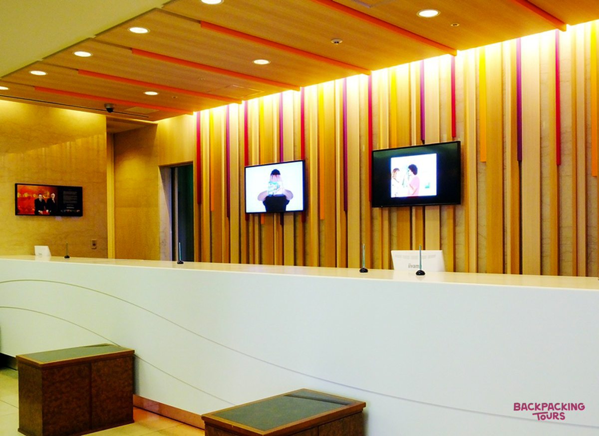 A modern hotel reception desk in Osaka with a curved white counter and screens on a wooden wall.