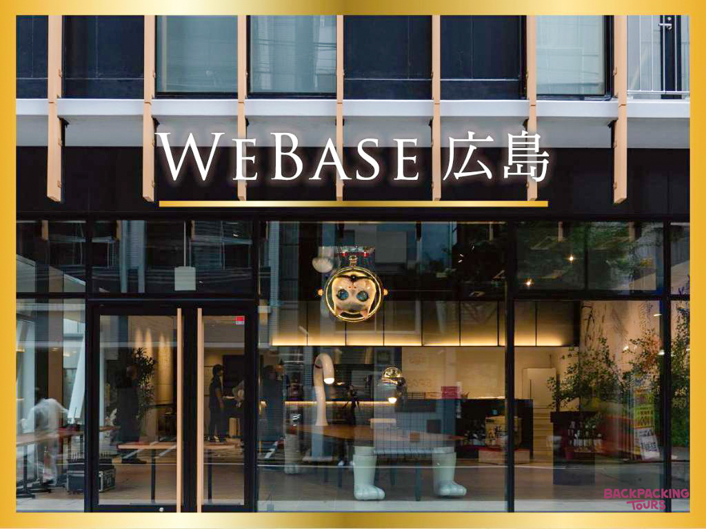 The modern entrance of WeBase Hiroshima, a stylish hostel with large glass windows.
