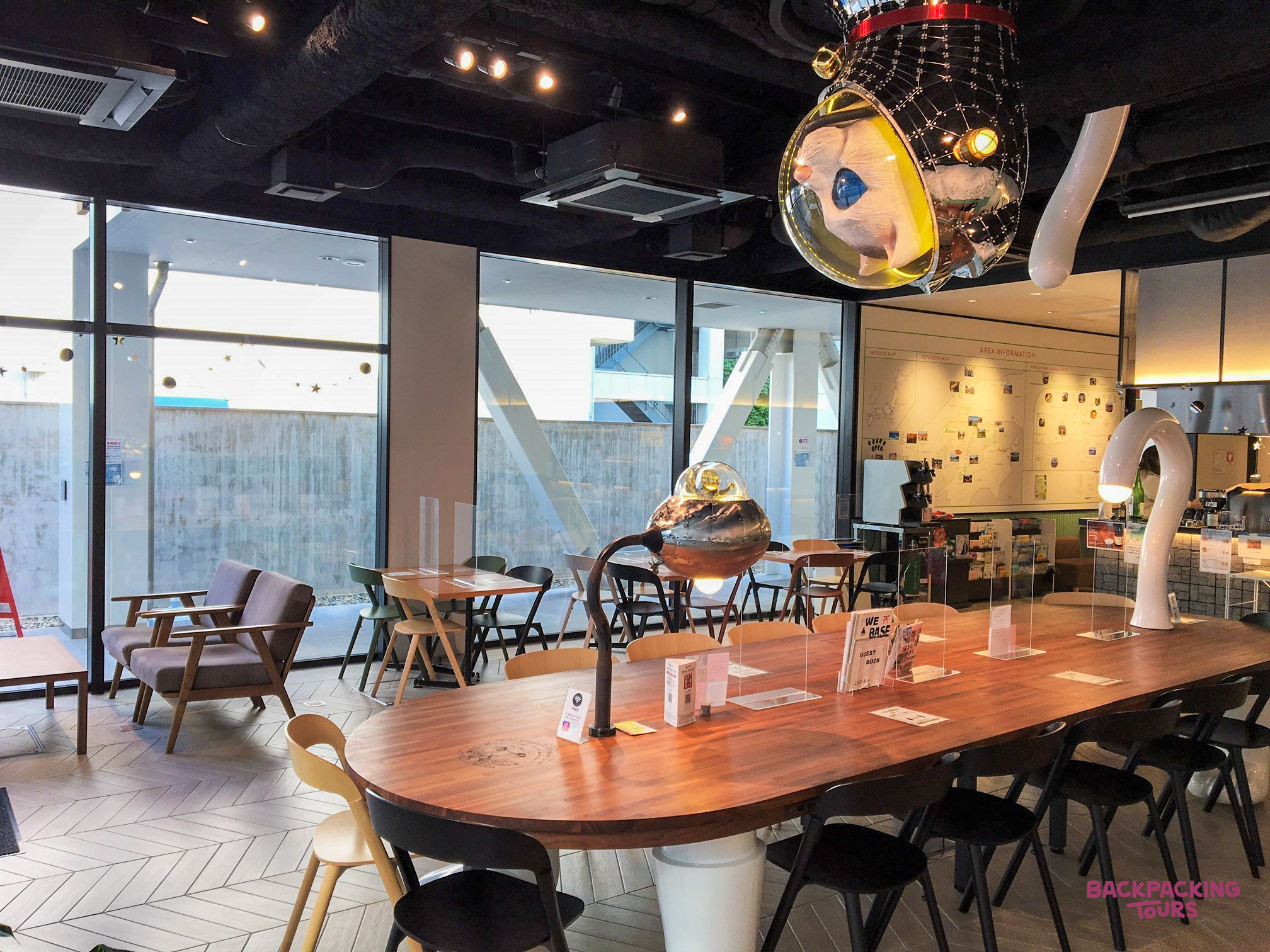 A contemporary hostel common room in Hiroshima with a long communal table and comfortable seating.