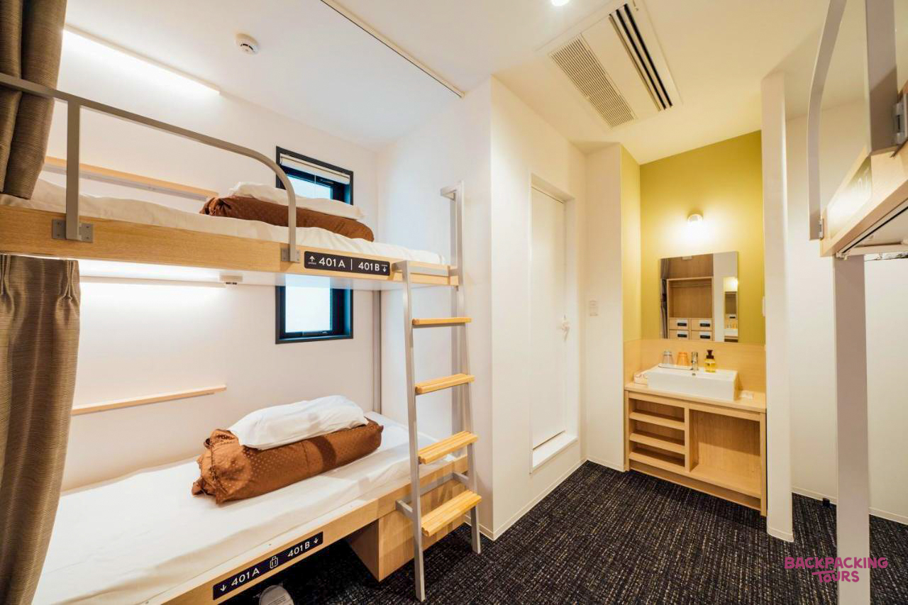 Clean, modern bunk beds and a wash basin in a shared hostel room in Hiroshima, Japan.