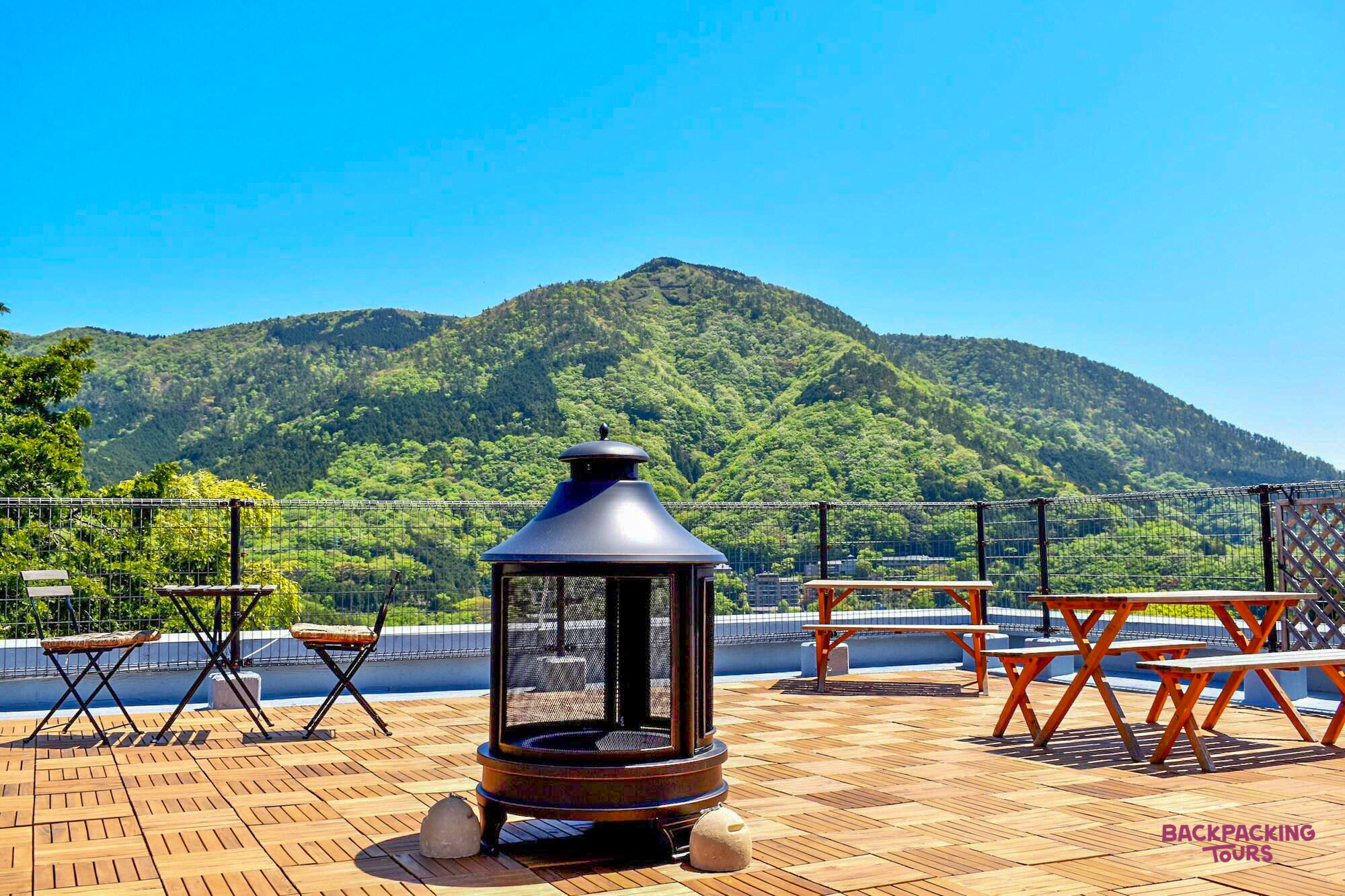 Rooftop deck of a mountain guesthouse in Hakone, offering stunning views of lush green peaks.