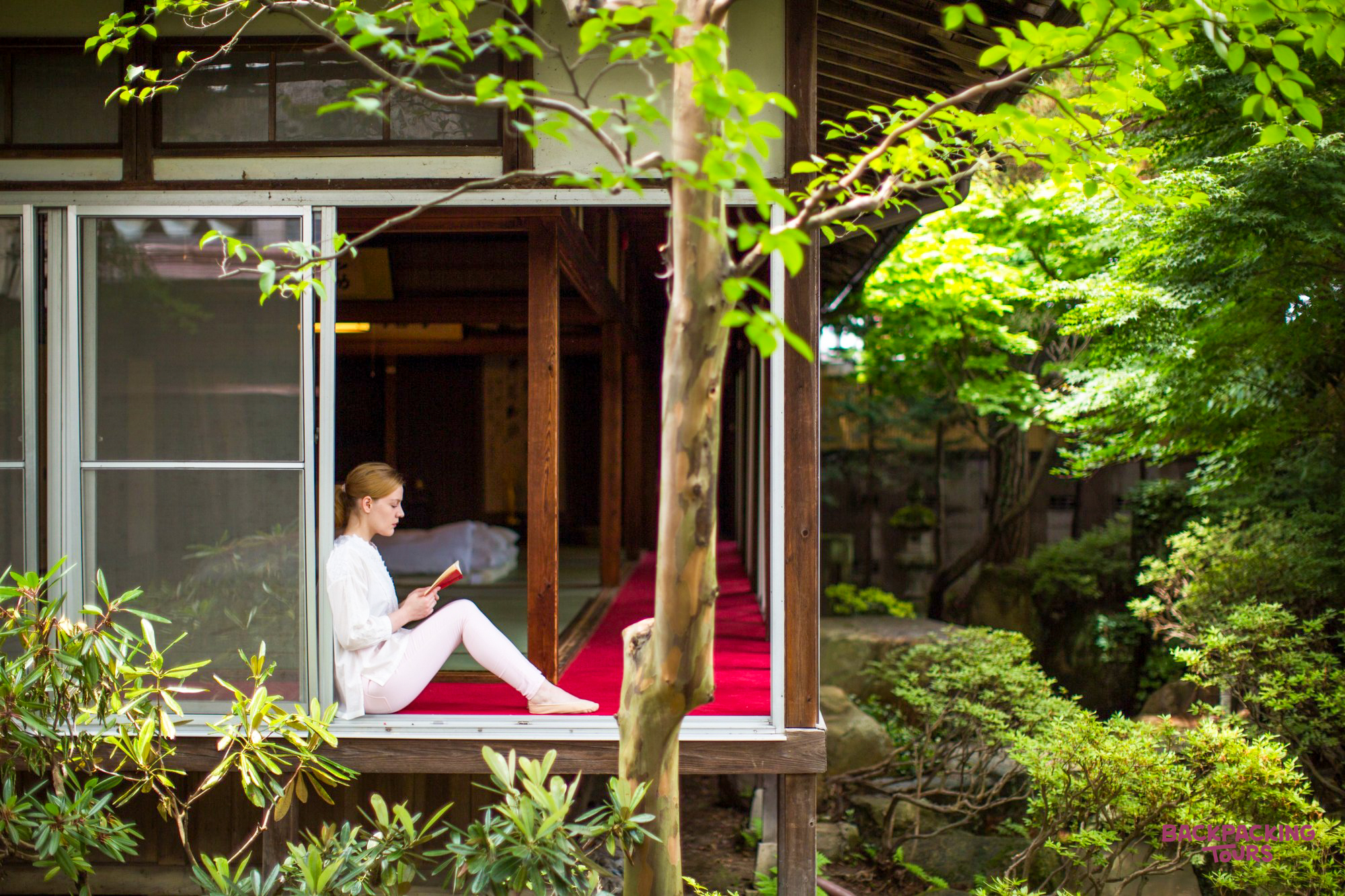A woman reads a book on a temple veranda overlooking a serene garden in Takayama, Japan.