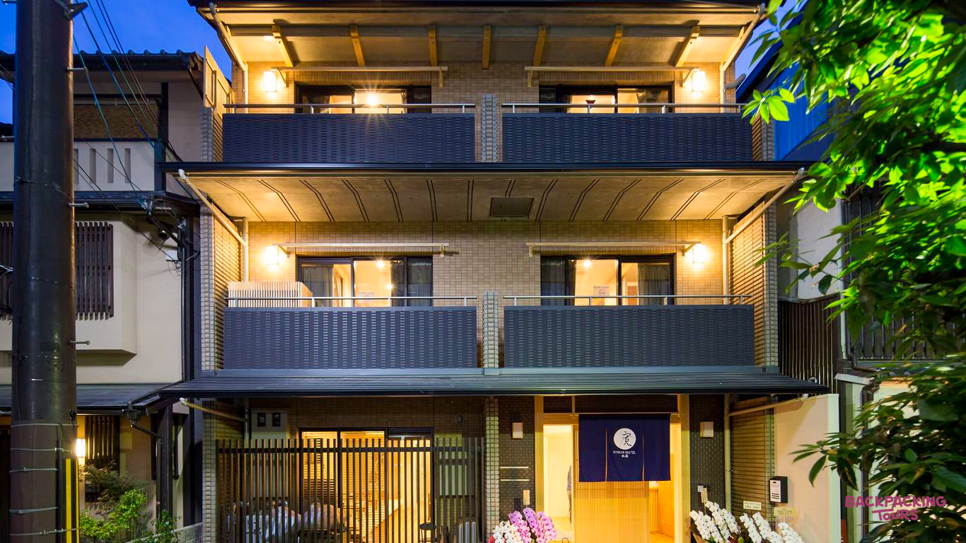 A charming Japanese ryokan hostel in Kyoto's Gion district, warmly lit at dusk.