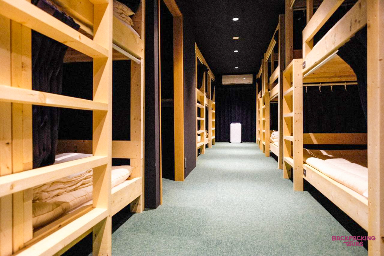A clean and modern hostel dormitory in Hiroshima with wooden bunk beds and green carpet.