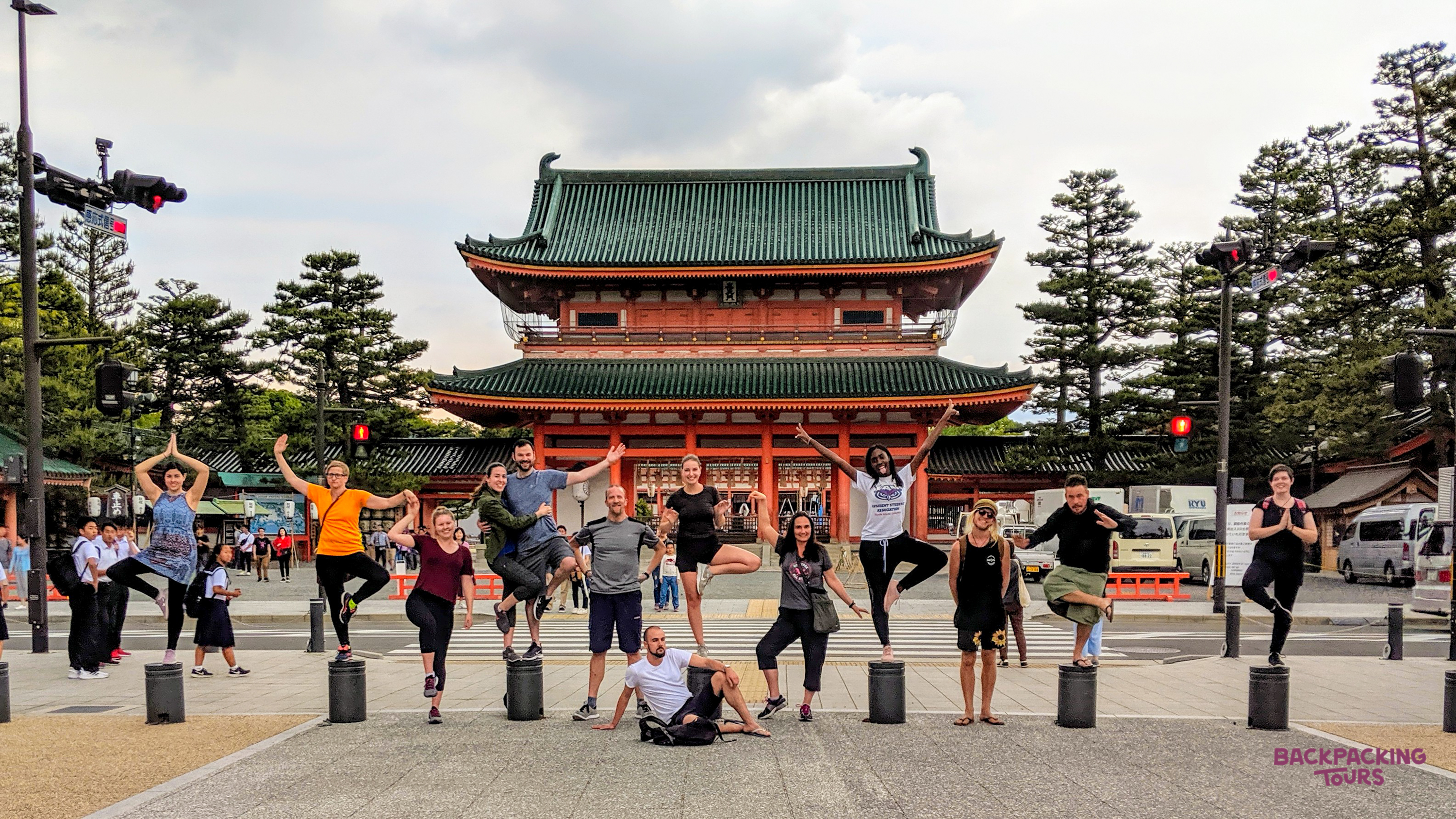 Backpackers strike playful poses on pillars in front of a grand traditional Japanese temple in Osaka.