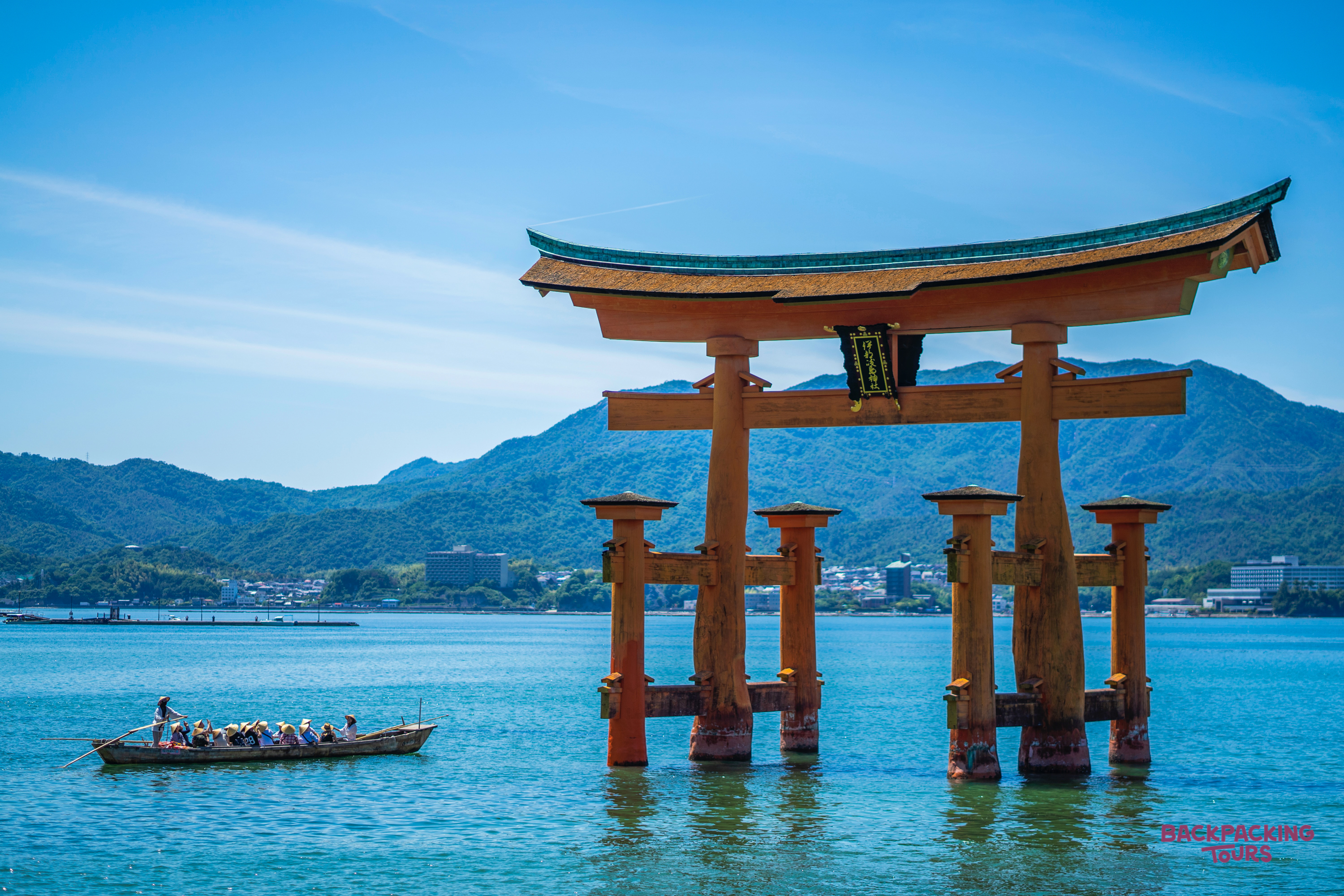 The iconic Great Torii Gate stands partly submerged in calm blue waters near Miyajima Island, Japan.