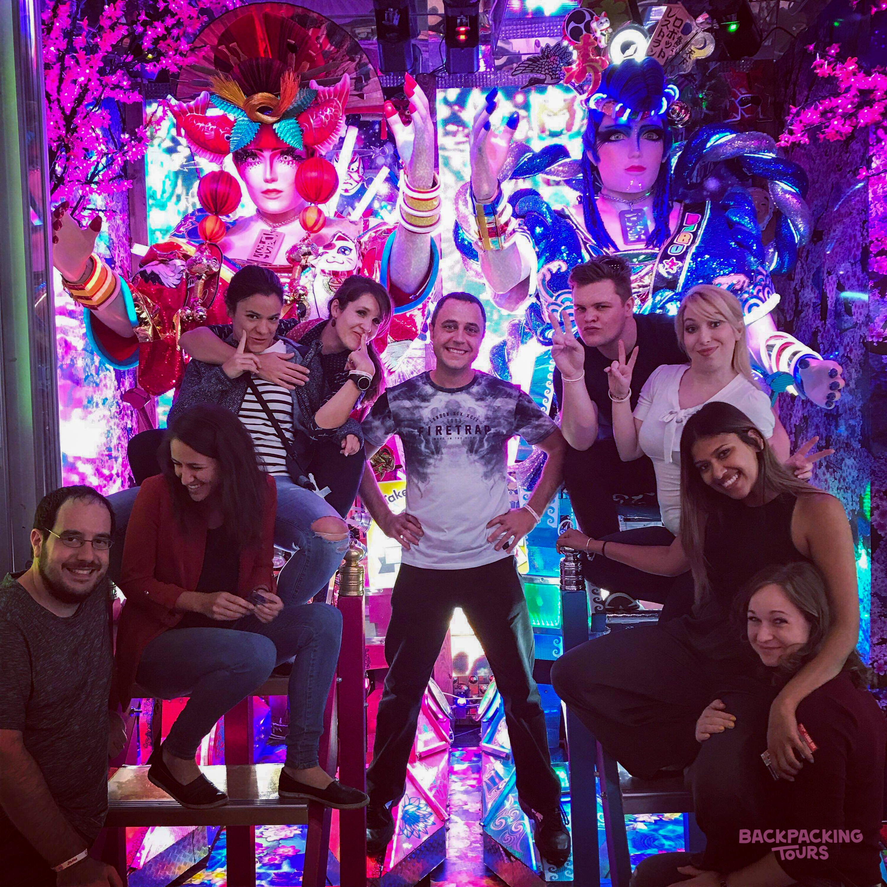 Backpacking group posing amid the colourful neon lights of an Akihabara arcade.