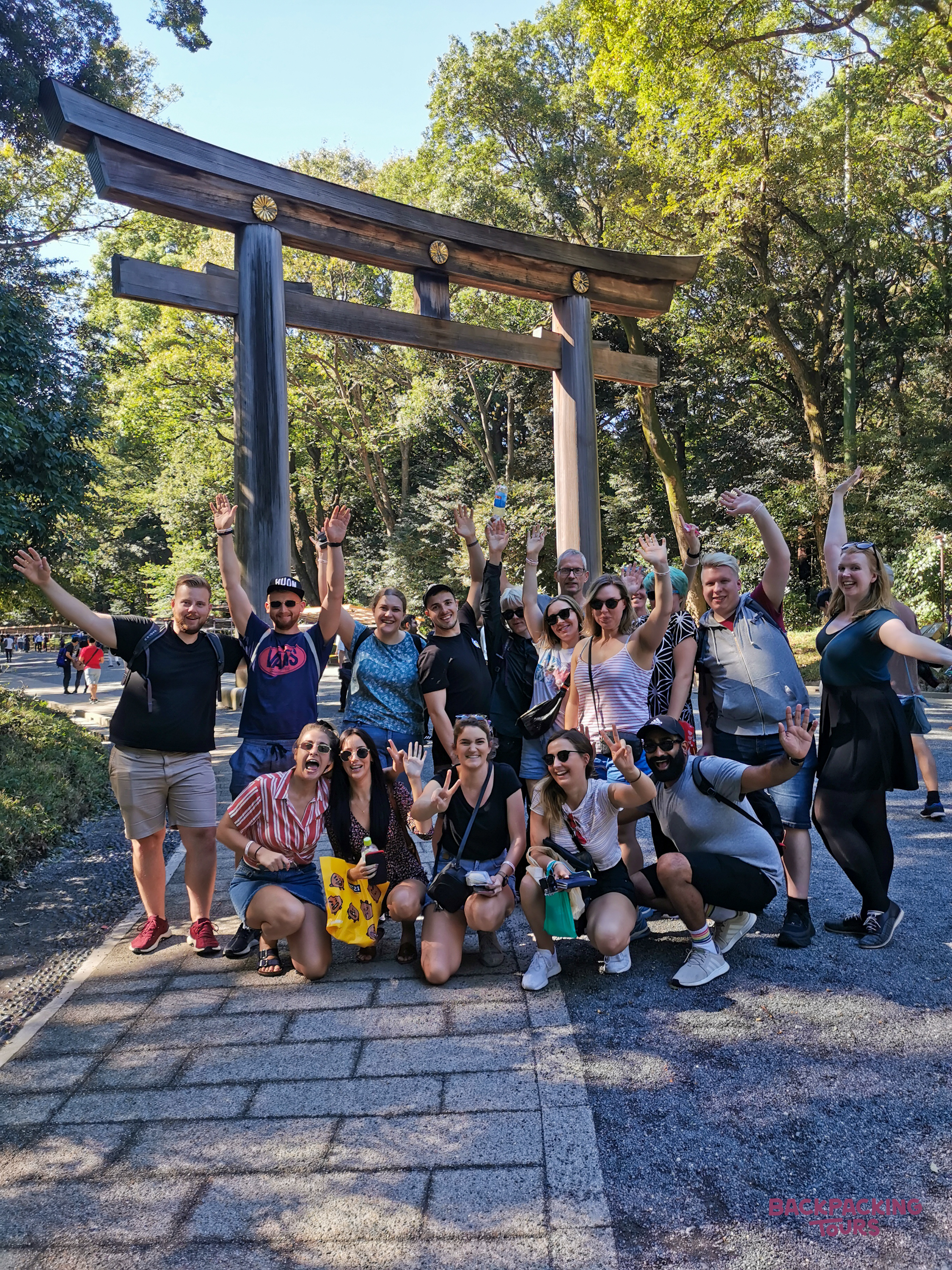 Smiling travelers pose enthusiastically before a grand torii gate at Meiji Shrine in Tokyo.