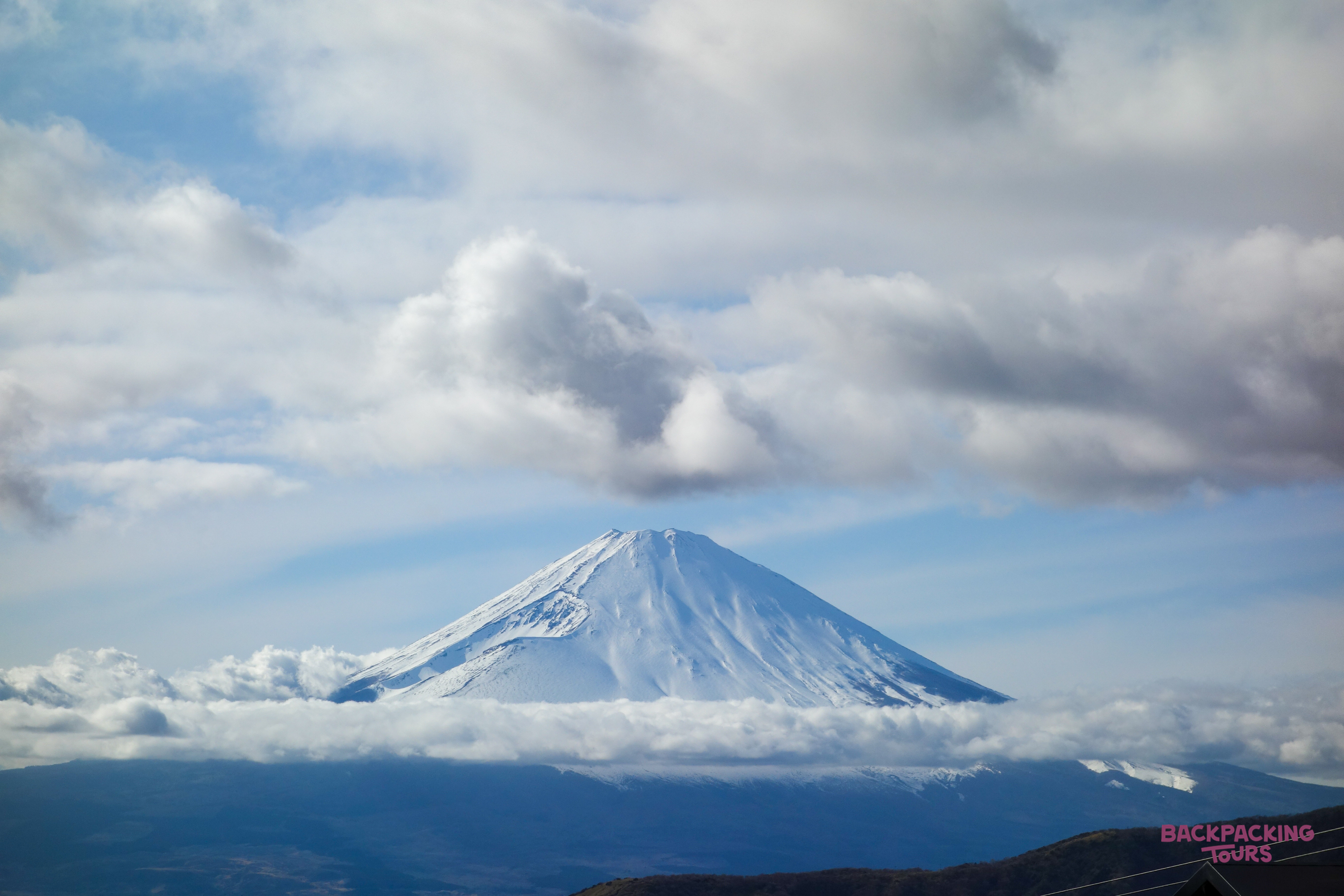 Majestic Mount Fuji, snow-capped and surrounded by fluffy clouds, stands tall against a blue sky.