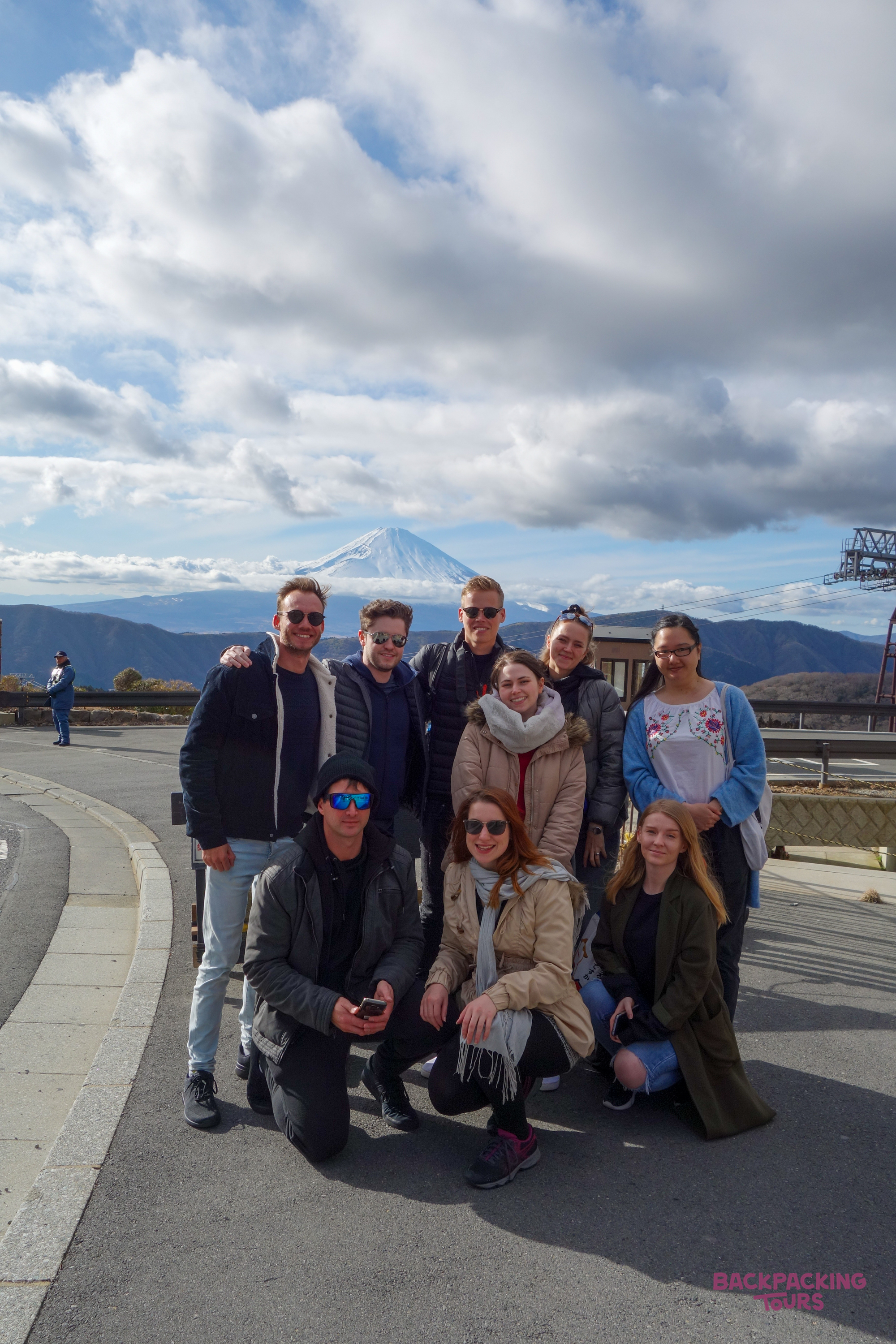 A group of happy backpackers posing together with the iconic snow-capped Mount Fuji in Hakone.