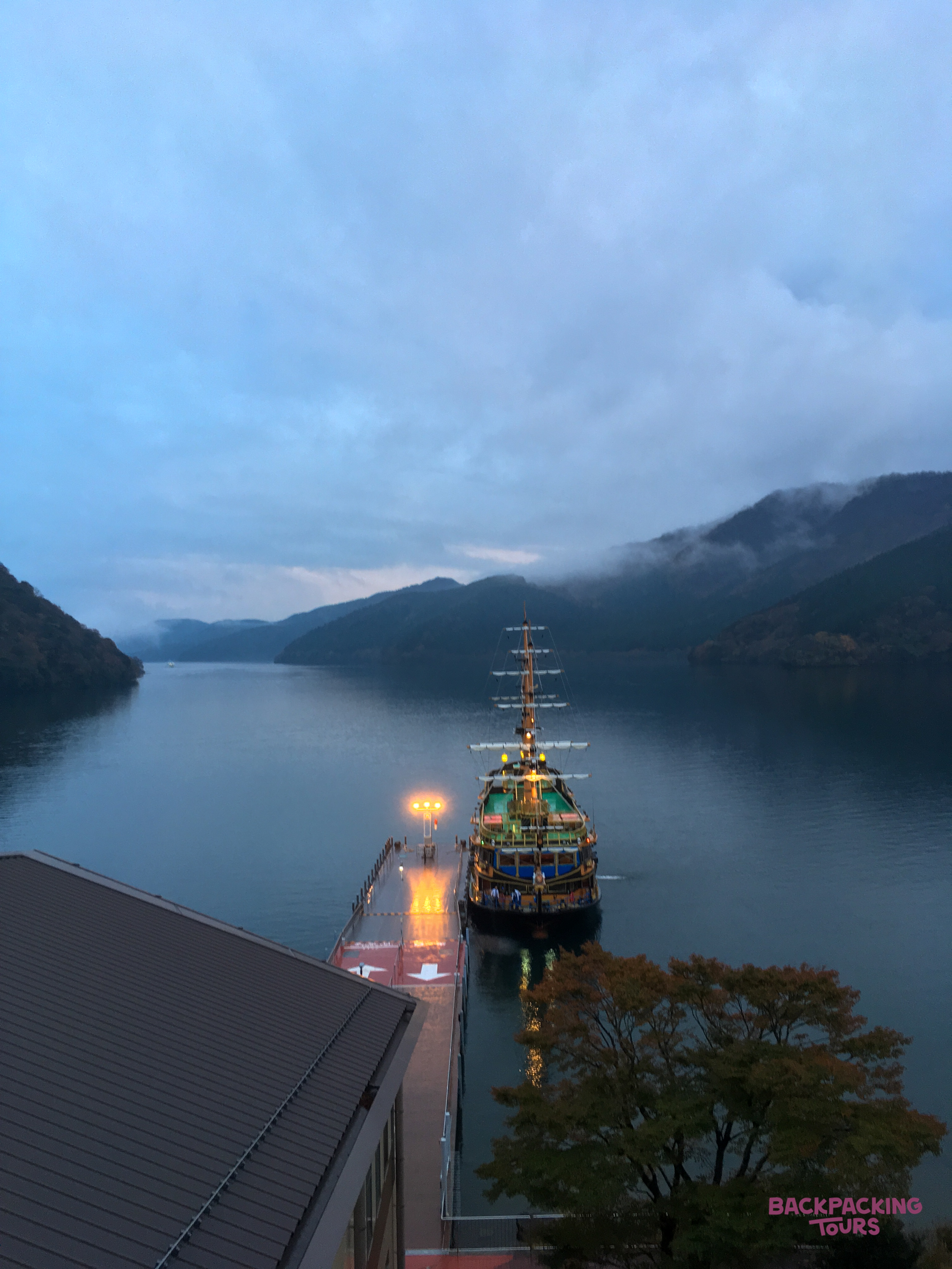 An illuminated pirate ship docked at a pier on Lake Ashi in Hakone, surrounded by misty mountains.