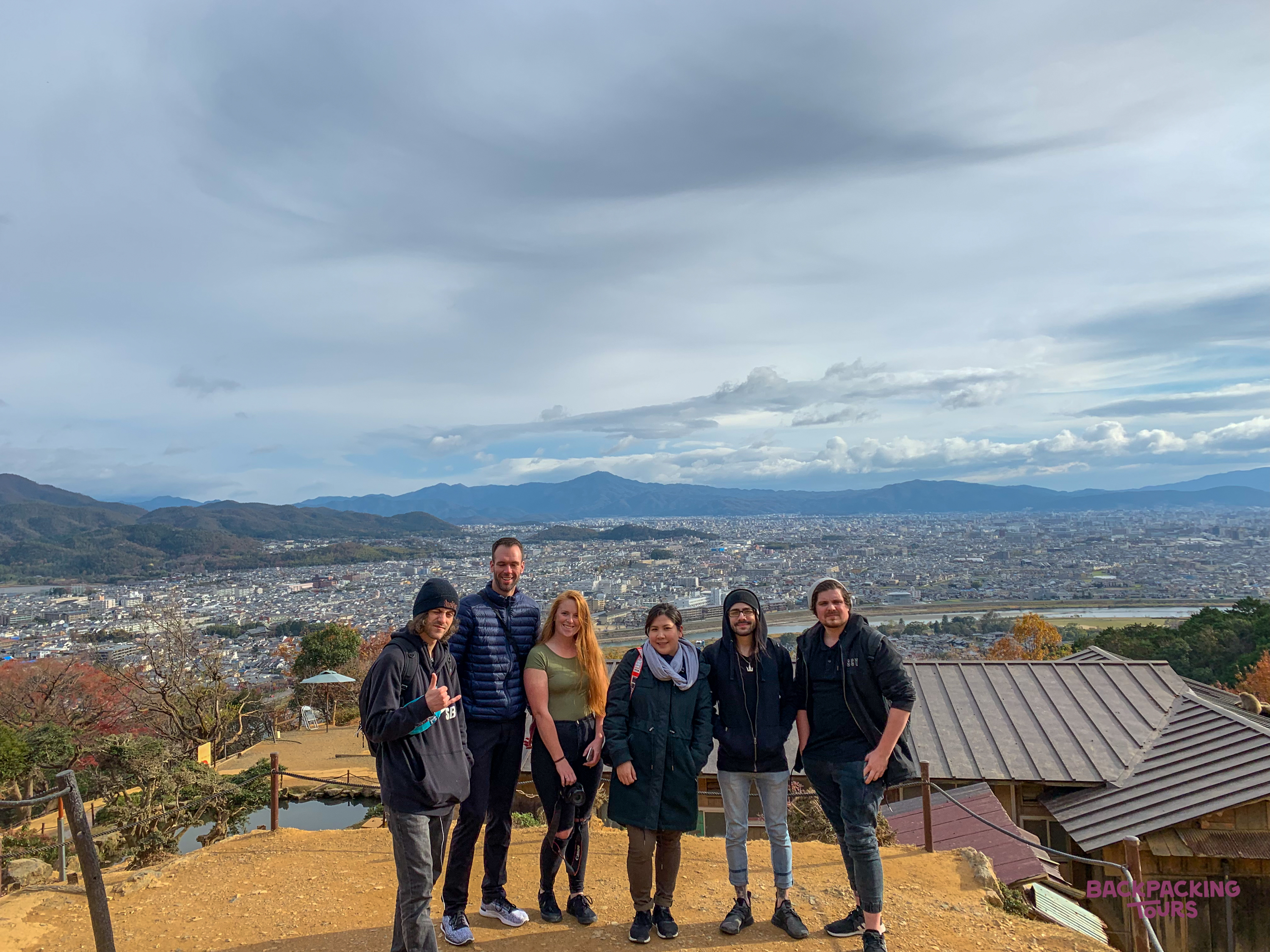Six happy backpackers pose on a hilltop overlooking the sprawling city of Hakone, Japan.