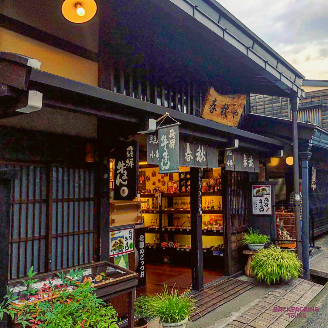 A charming traditional Japanese shop with warm lighting and plants on a quiet street in Takayama.