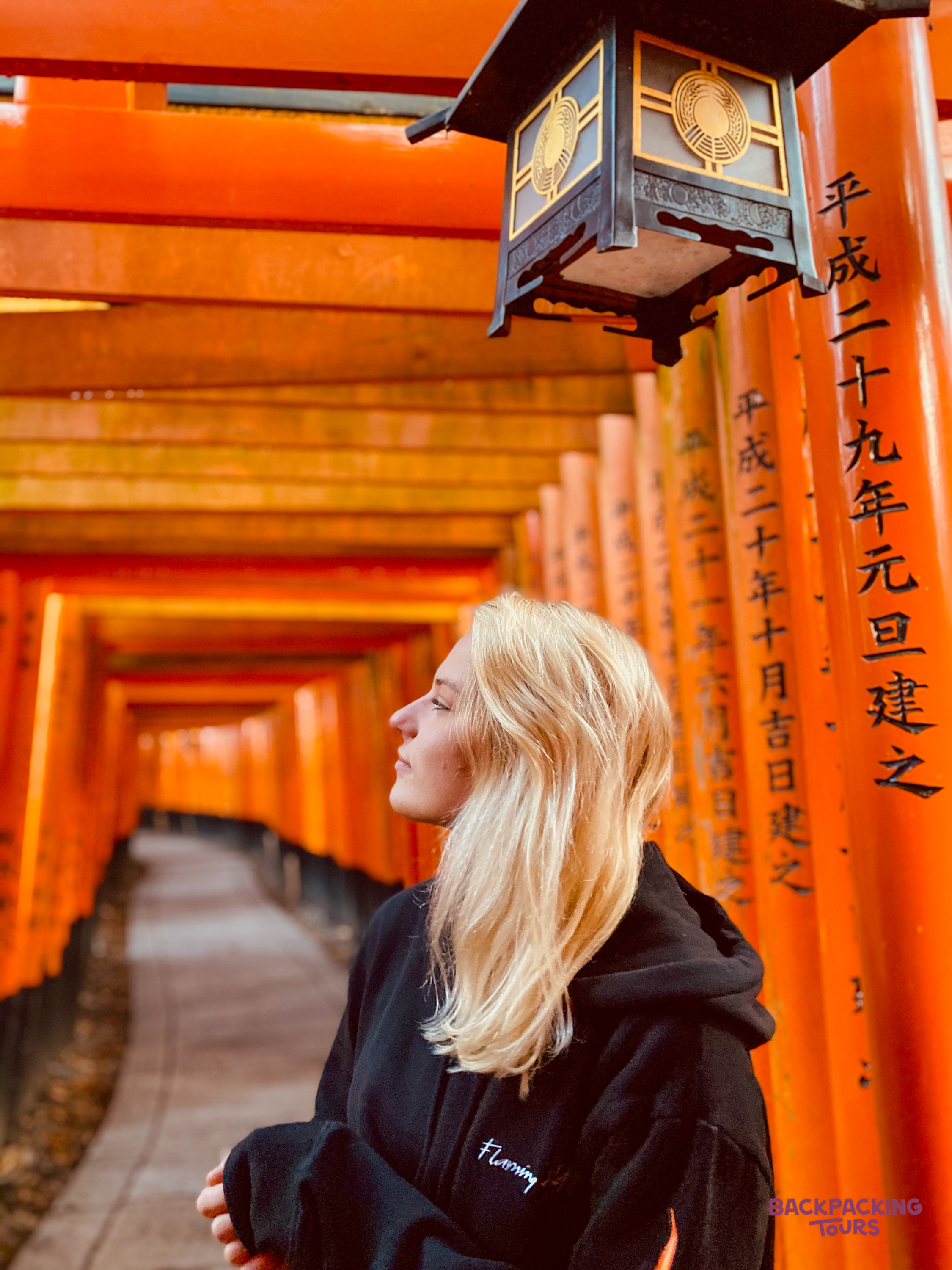 A young woman looks up, admiring the vibrant orange torii gates at Fushimi-Inari Shrine in Kyoto.