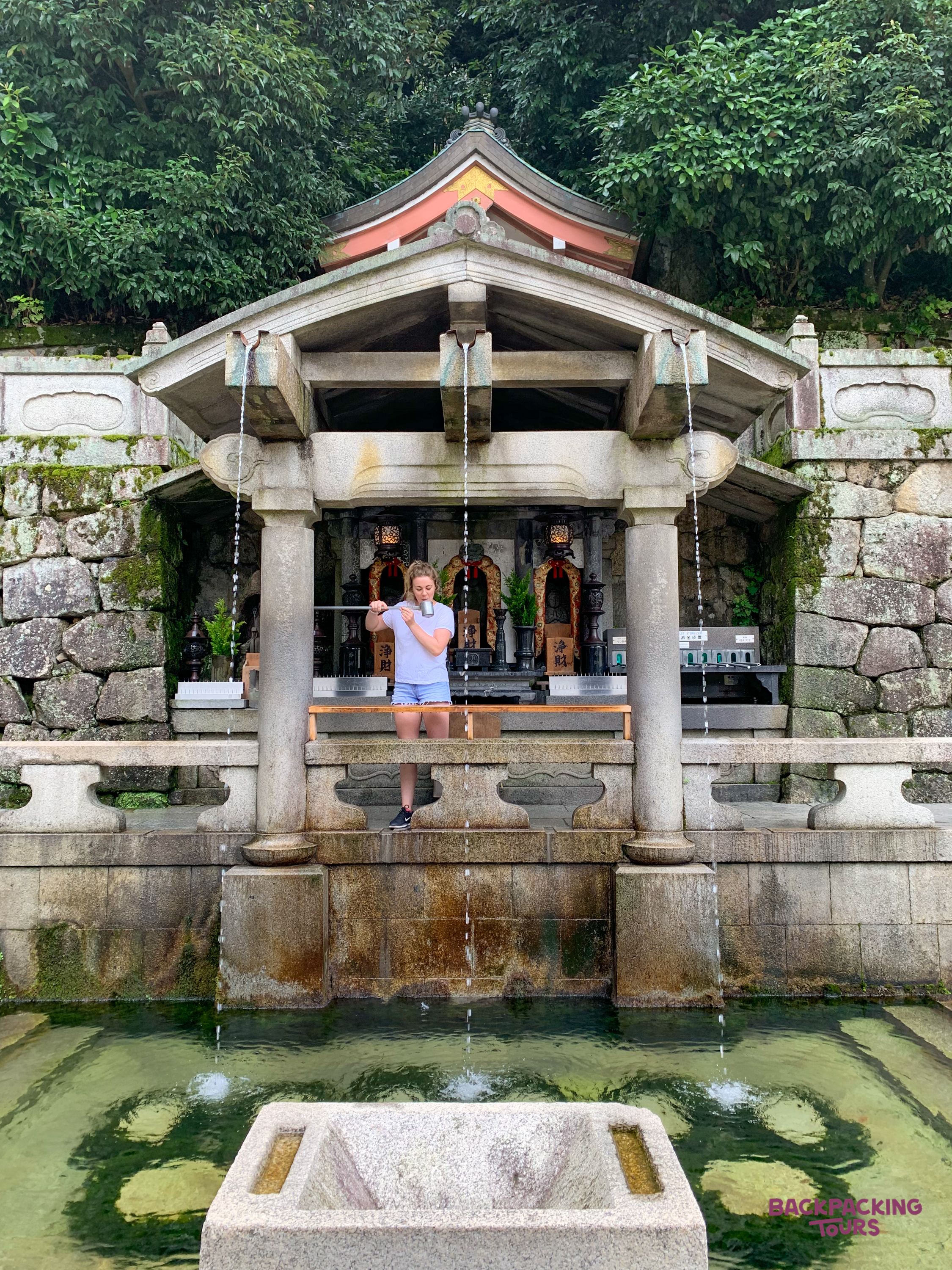 A backpacker collects water from a stone purification fountain at a temple in Kyoto.