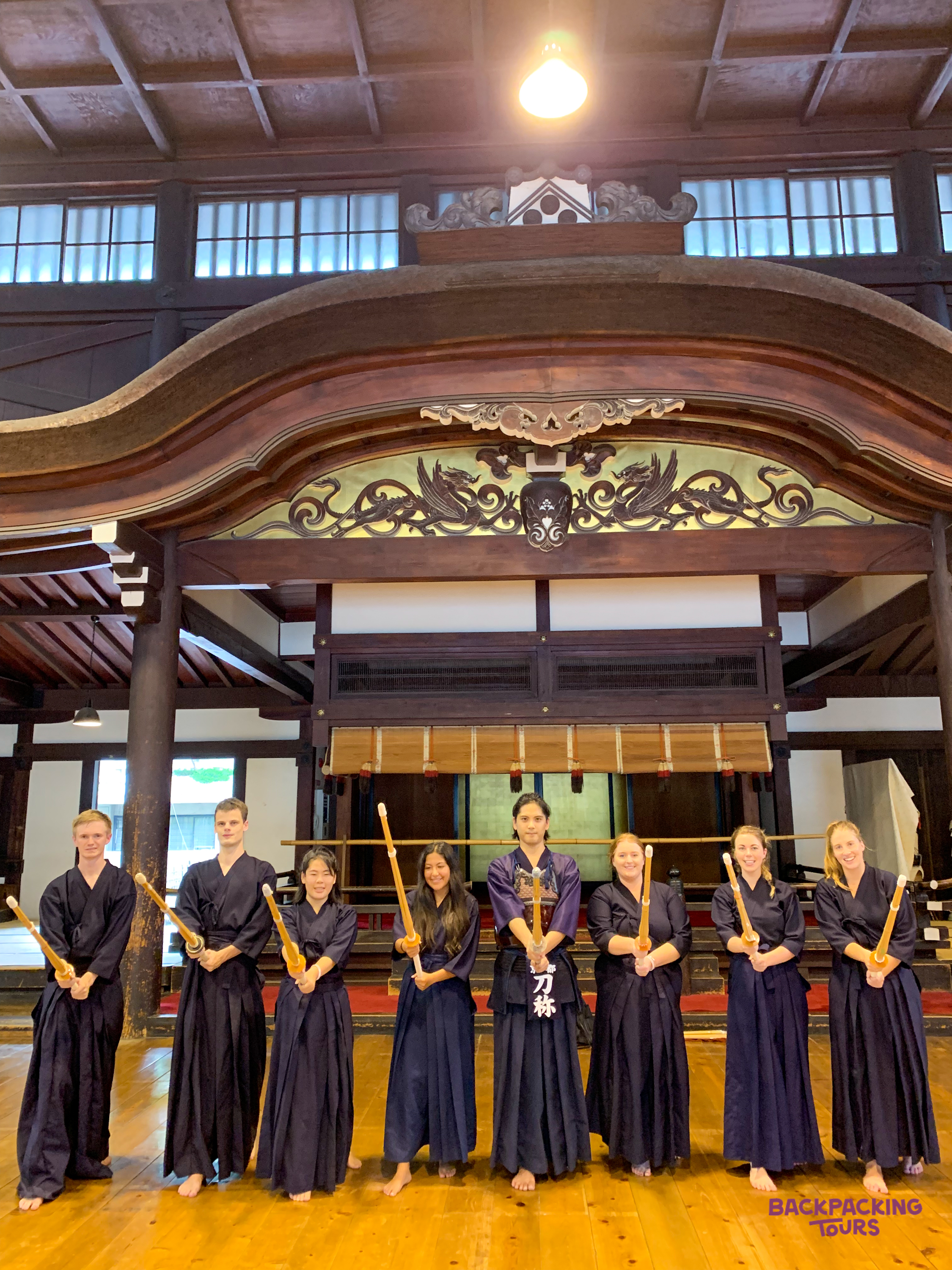 Travelers in traditional Japanese clothing proudly hold wooden swords during a Kendo class in Kyoto.