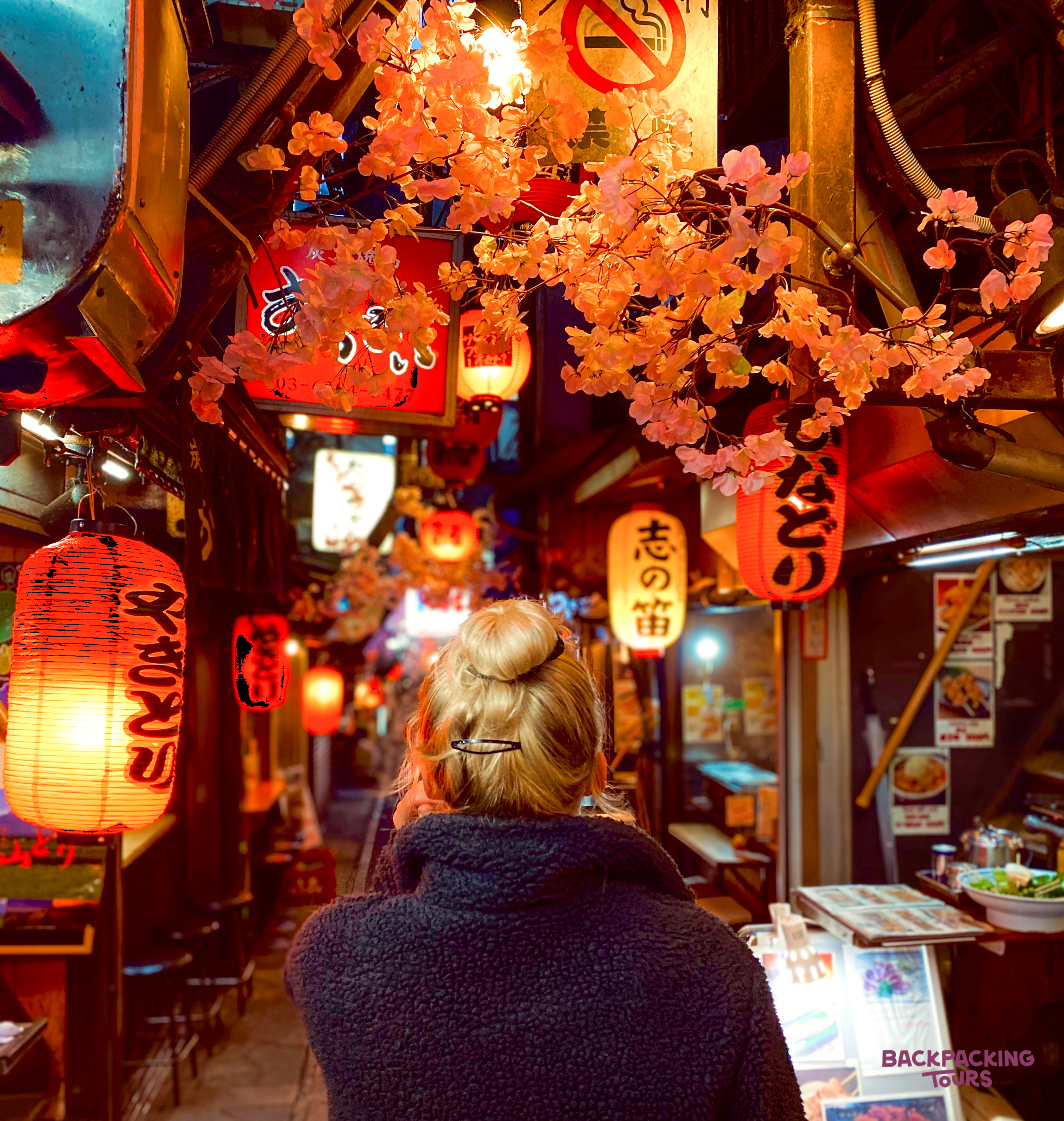 A person walks through a vibrant Osaka alley, lit by glowing red lanterns and cherry blossoms.