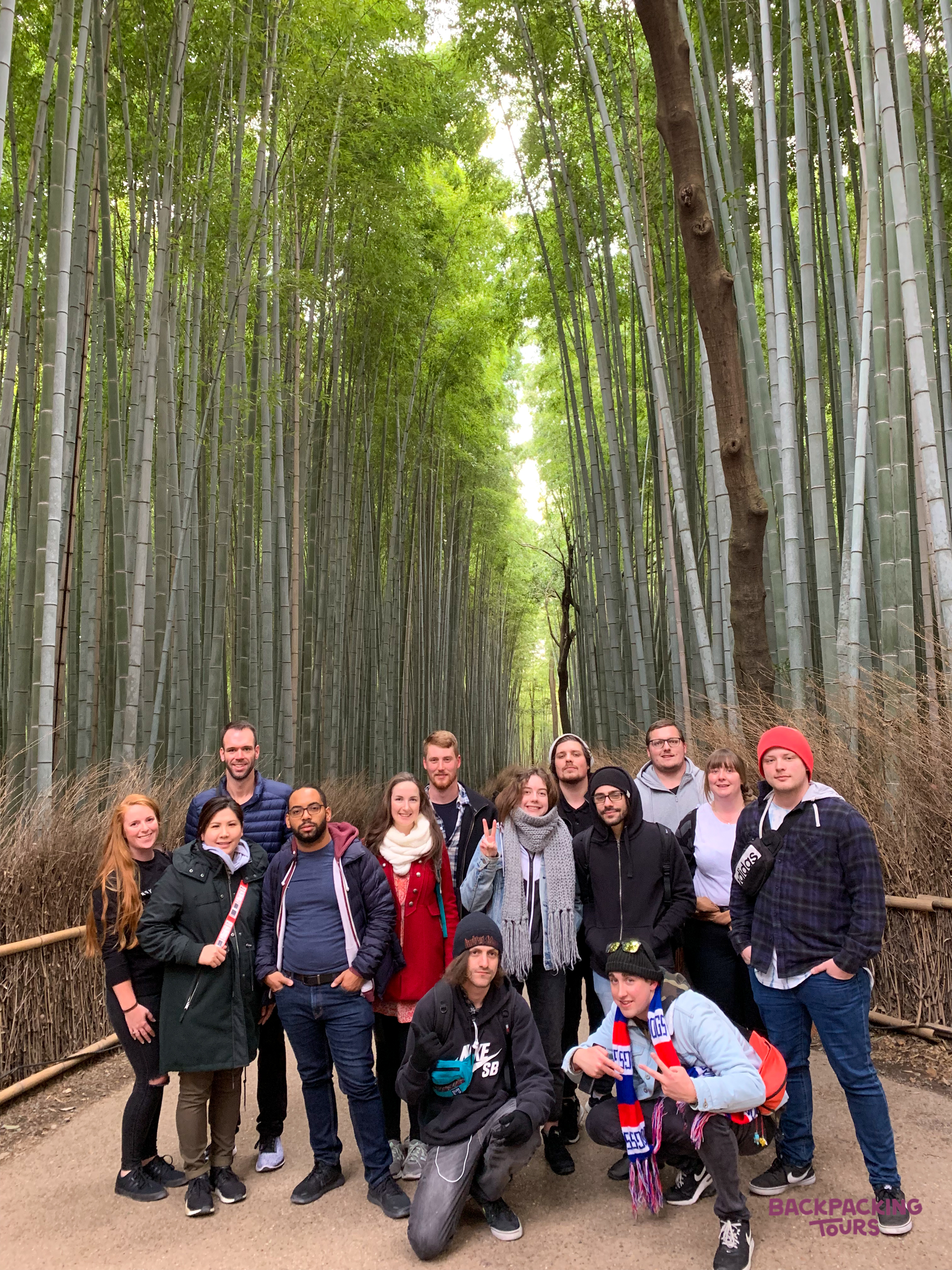 A group of happy backpackers posing together in the stunning Arashiyama Bamboo Grove, Japan.