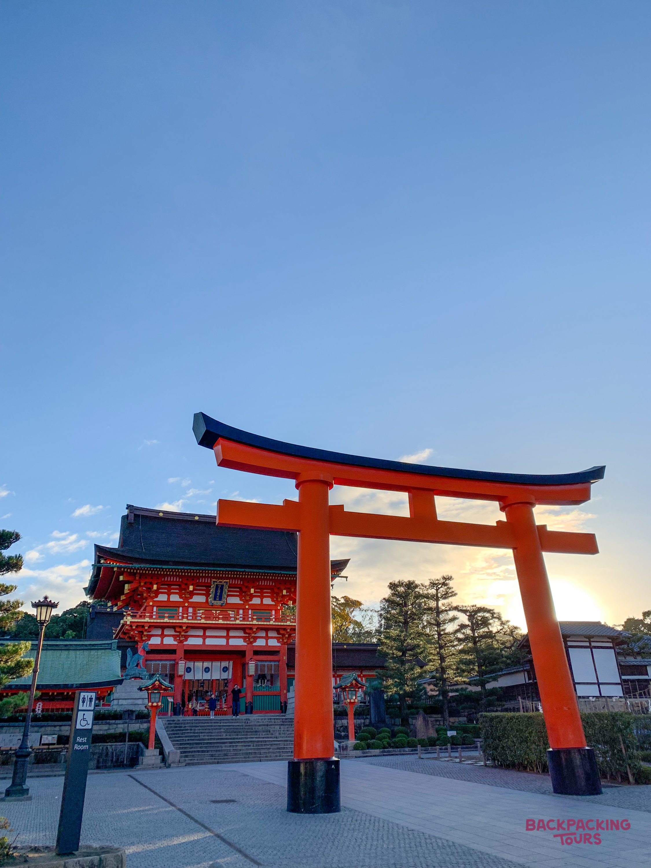 The iconic orange torii gate welcomes visitors to a stunning Japanese temple at sunset.