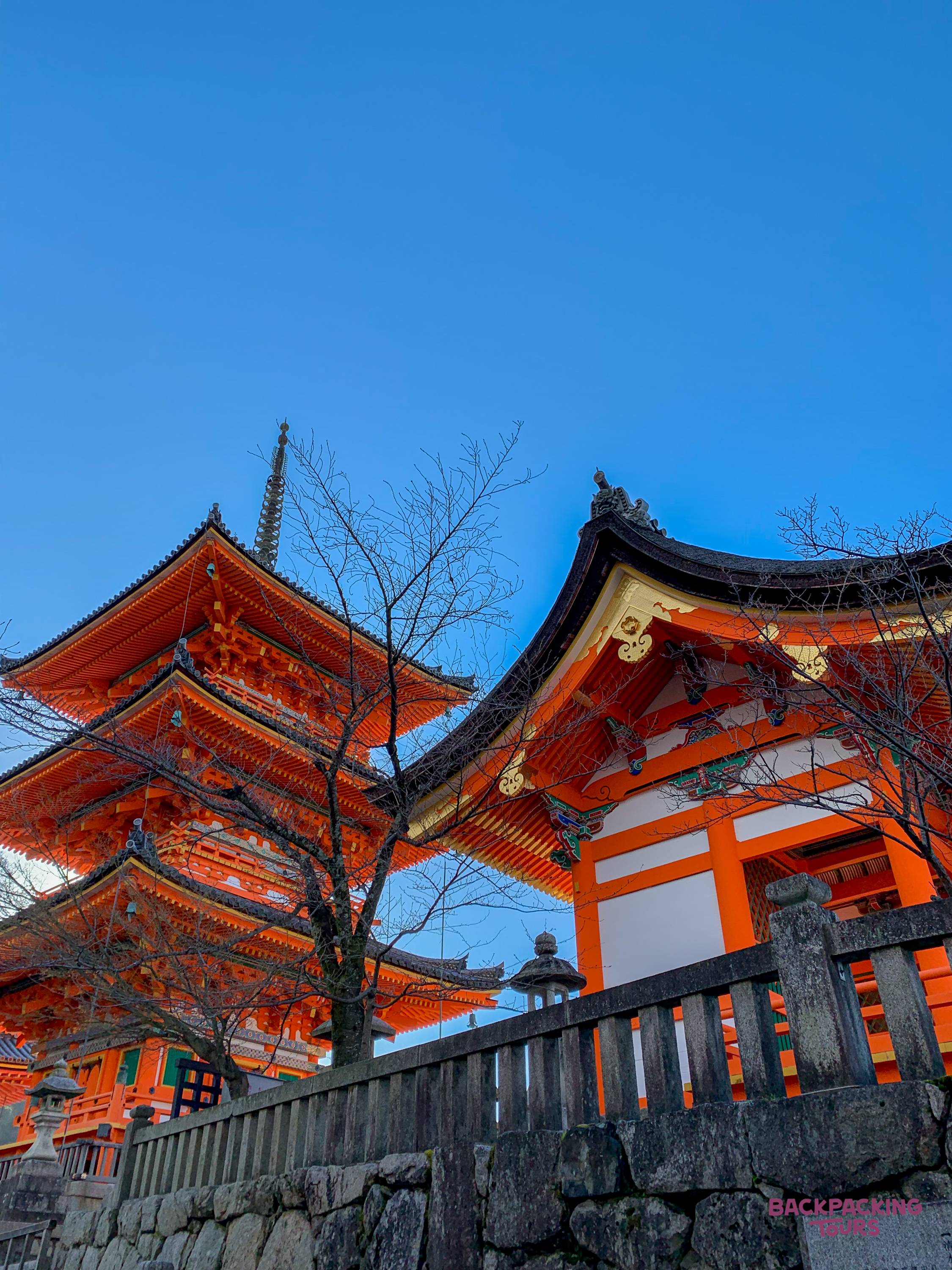 Vibrant orange pagoda and temple buildings stand against a clear blue sky in Tokyo.