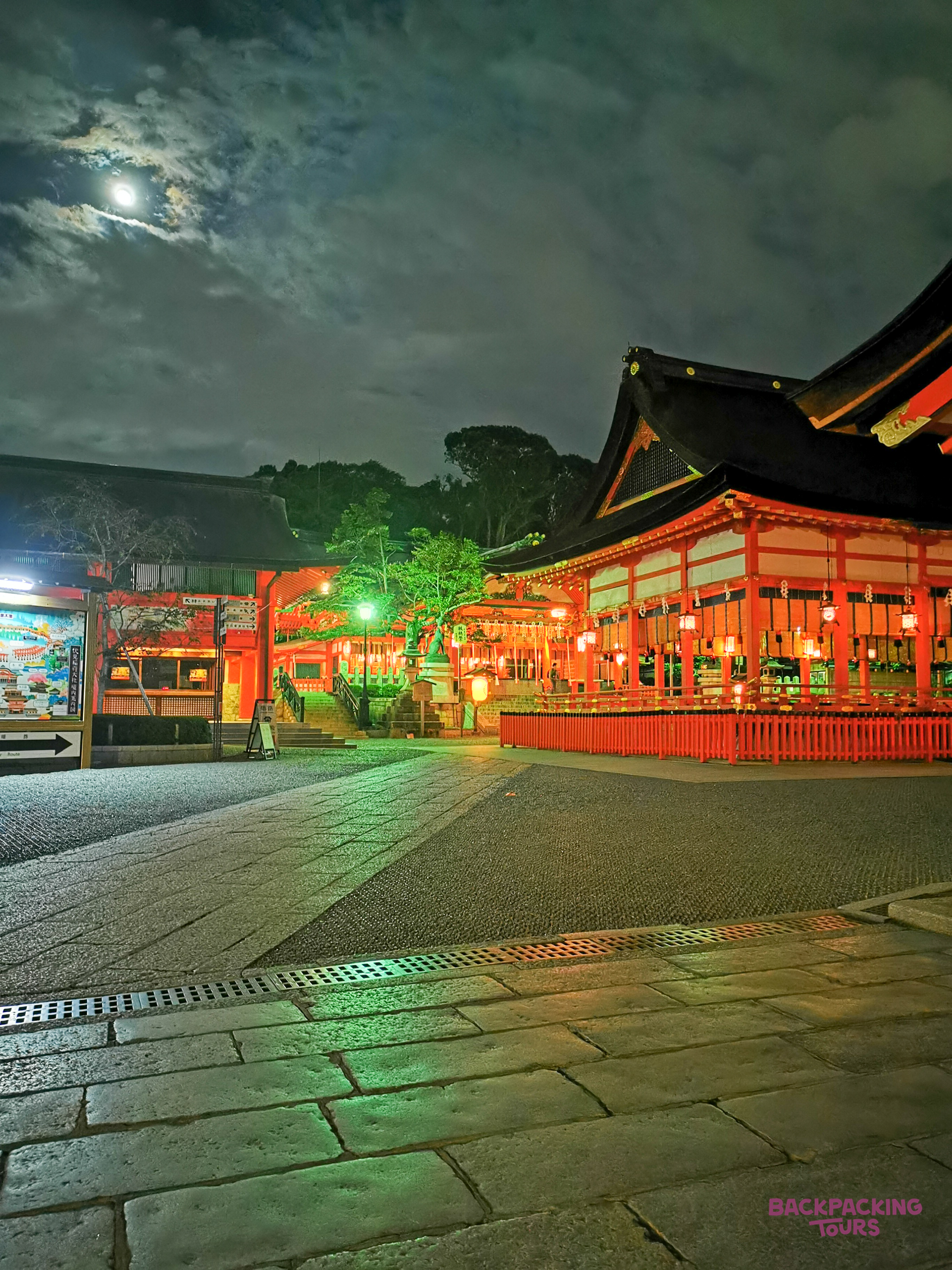 The iconic Senso-ji Temple in Tokyo shines brightly with red lights under a full moon at night.