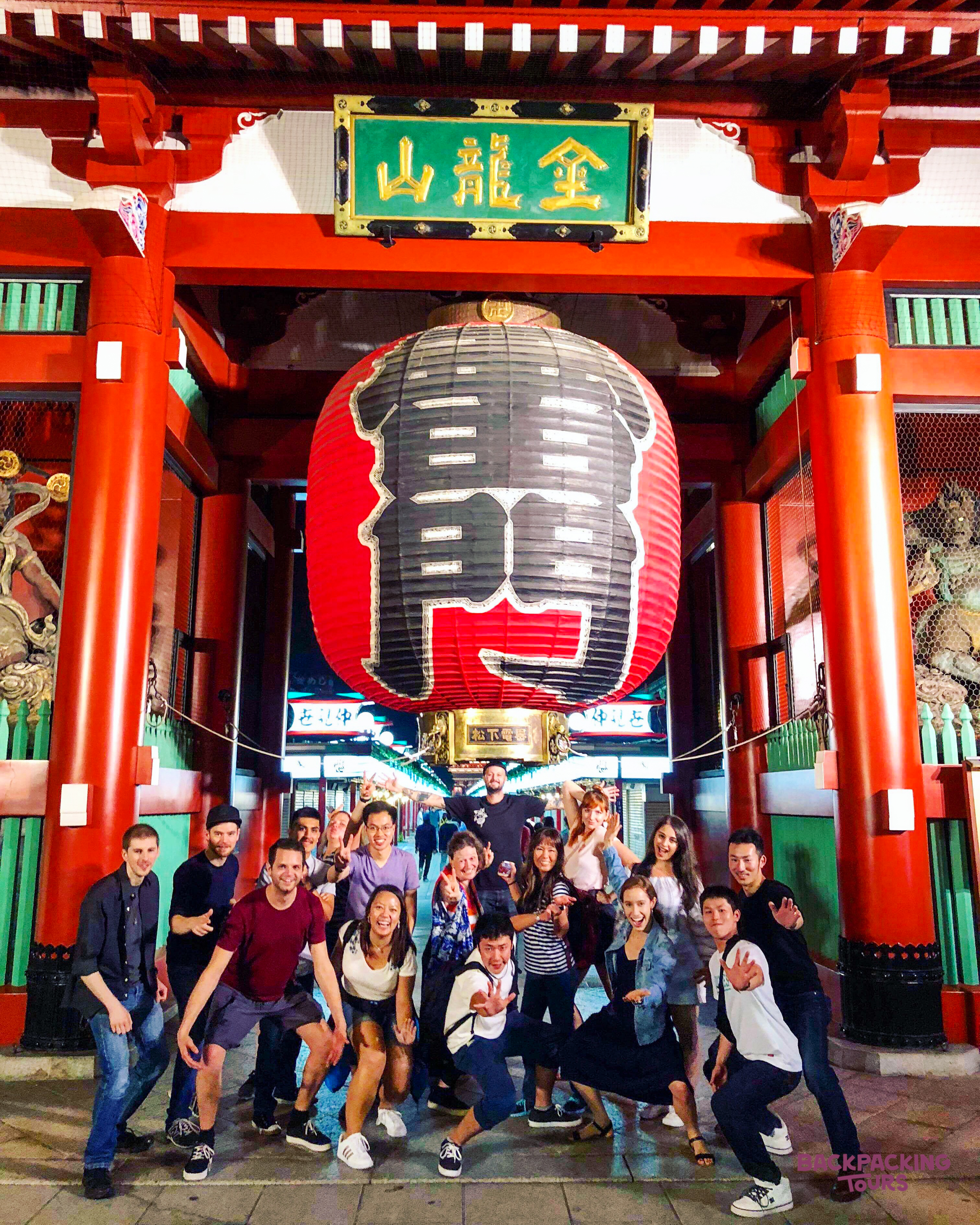 Smiling backpackers strike a pose under the famous Kaminarimon Gate lantern at Senso-ji Temple, Tokyo.