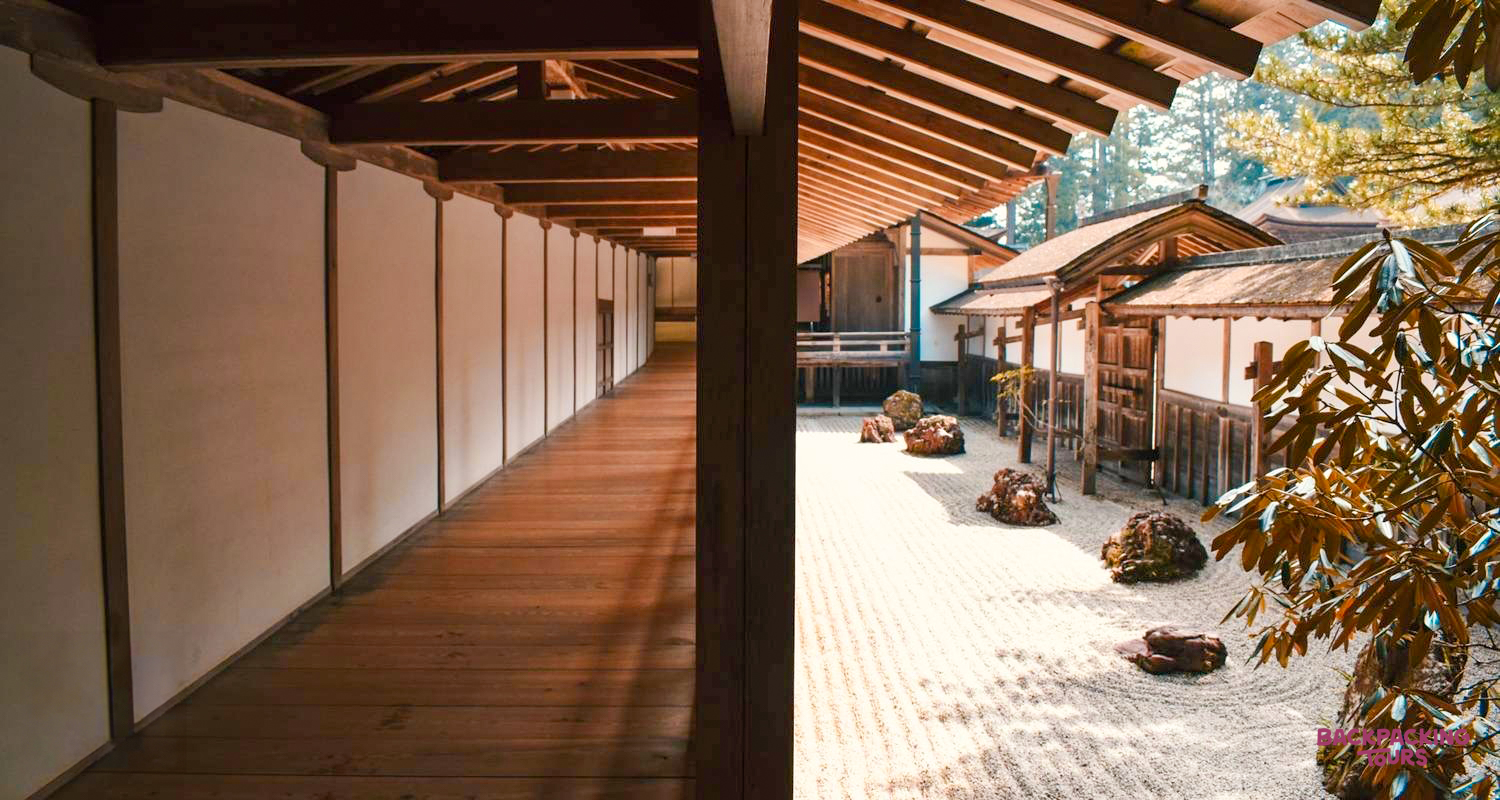 A serene dry garden with raked sand and rocks beside a traditional wooden temple corridor in Koyasan.