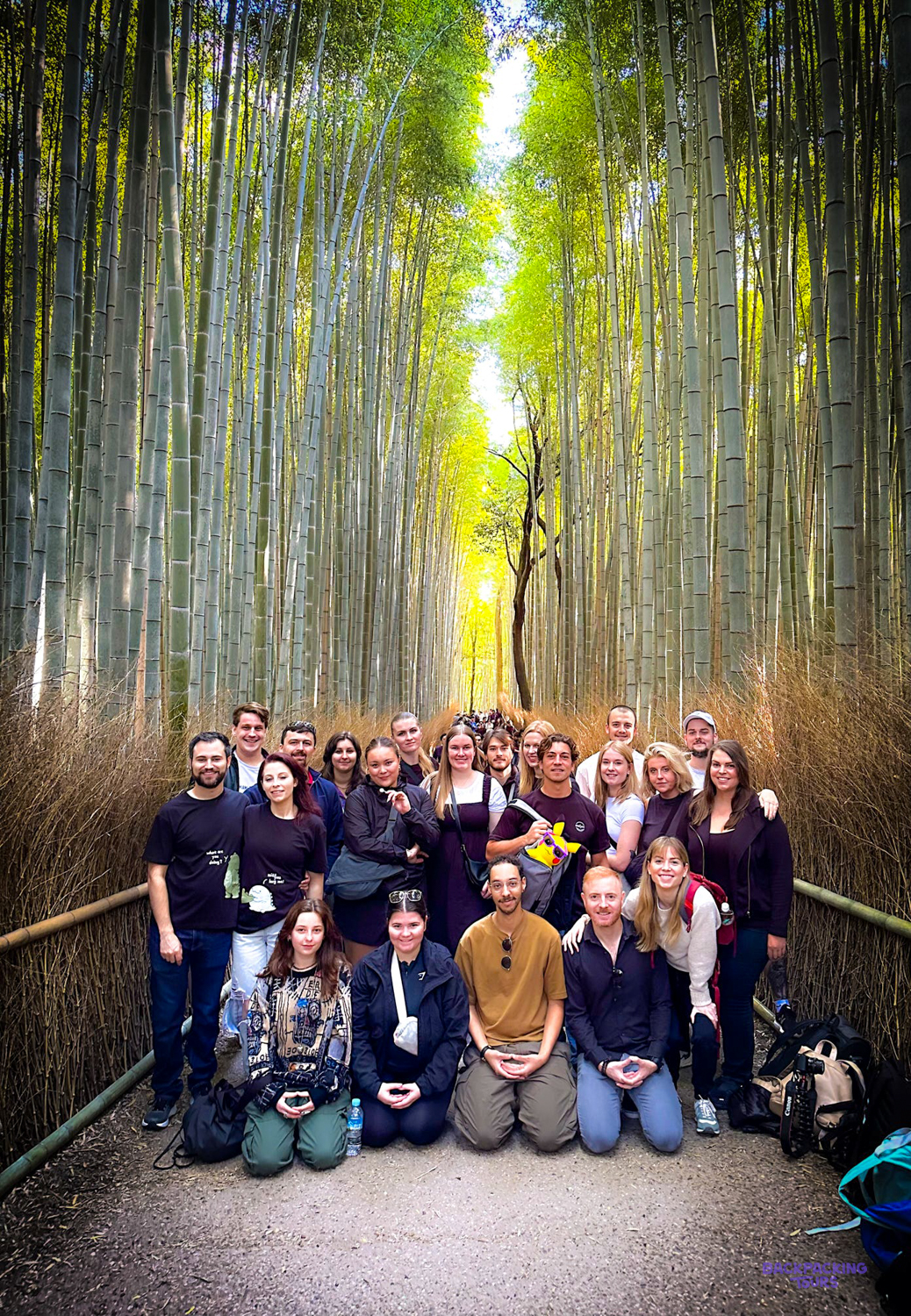 Backpacking group surrounded by the towering green stalks of Arashiyama Bamboo Grove.