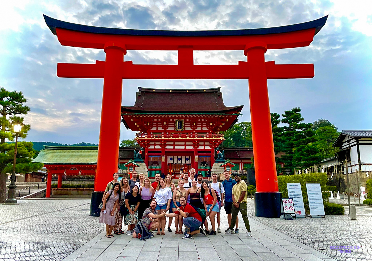 Backpacking group posing beneath the vivid red torii gates of Fushimi Inari Taisha shrine.