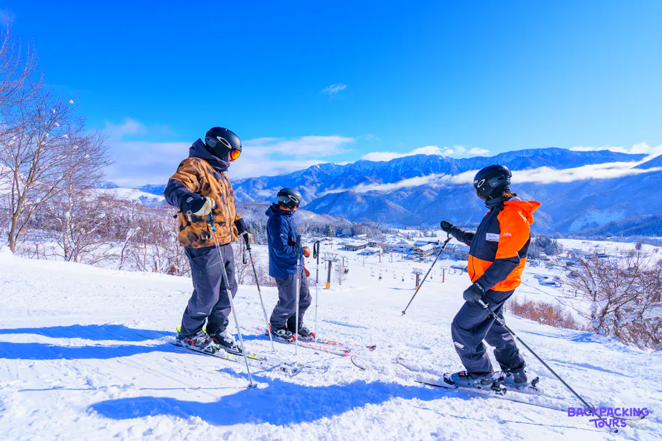 Three skiers on a sunny Hakuba mountain slope, enjoying the clear blue sky and snowy peaks.