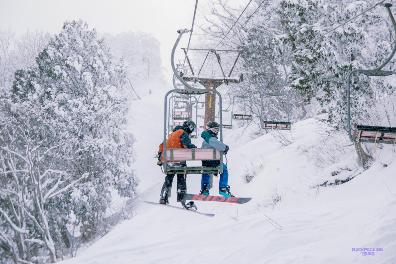 Skiers riding a snowy chairlift up the slopes near Nagano's ski fields.