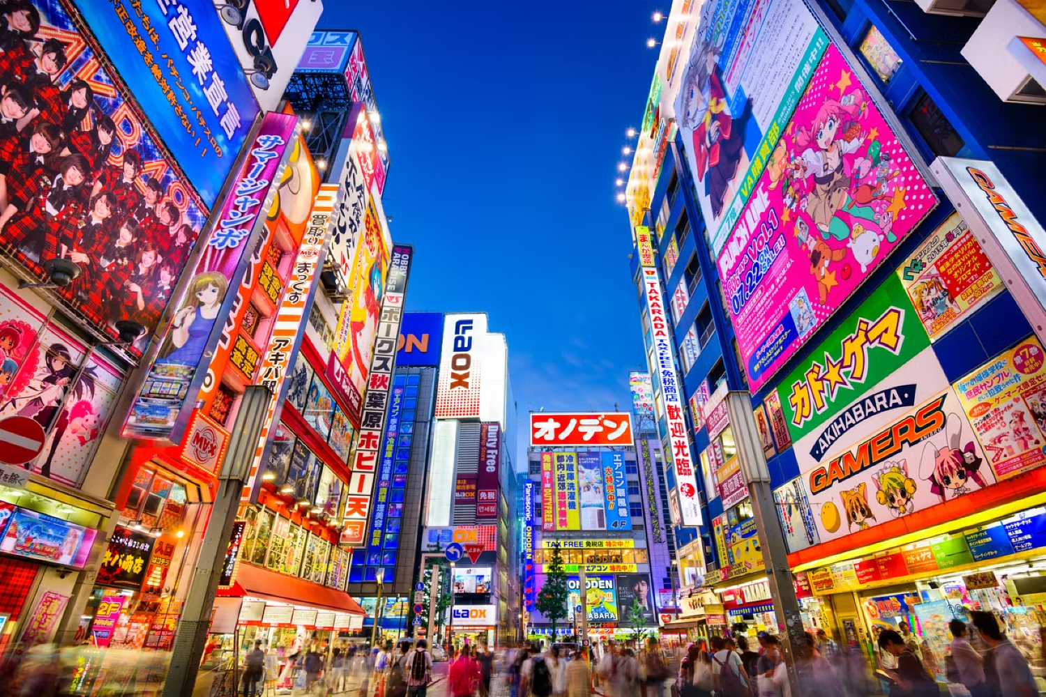 Vibrant Akihabara street at night, illuminated by colorful neon signs and bustling with pedestrians.