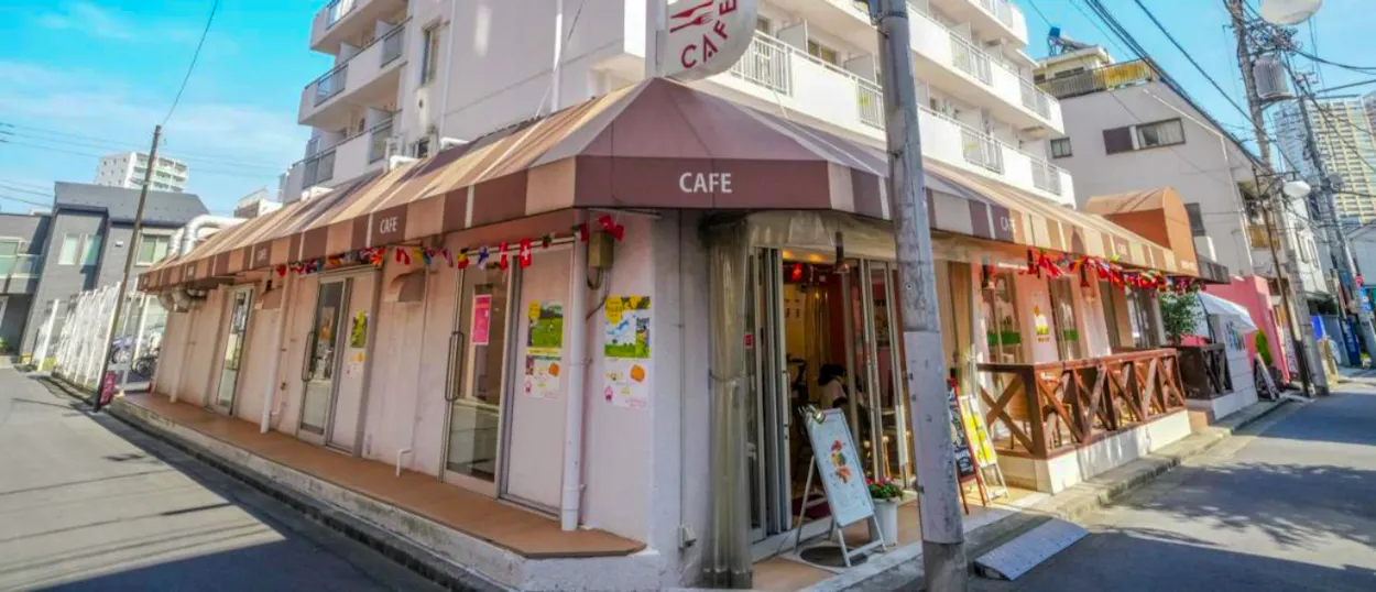 A charming corner cafe with striped awnings and outdoor seating on a sunny street in Tokyo.