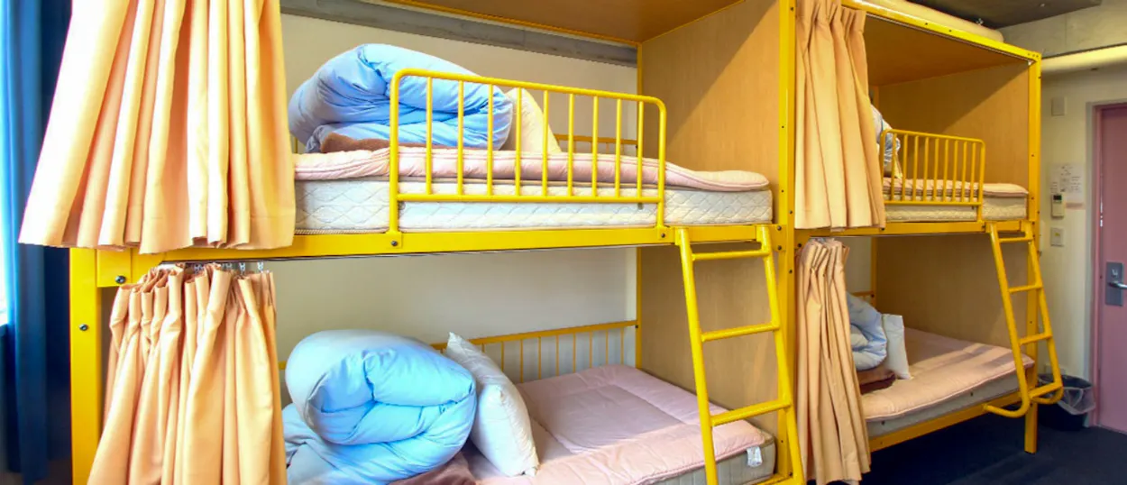 Bright yellow bunk beds with privacy curtains and rolled duvets in a Tokyo hostel dorm.