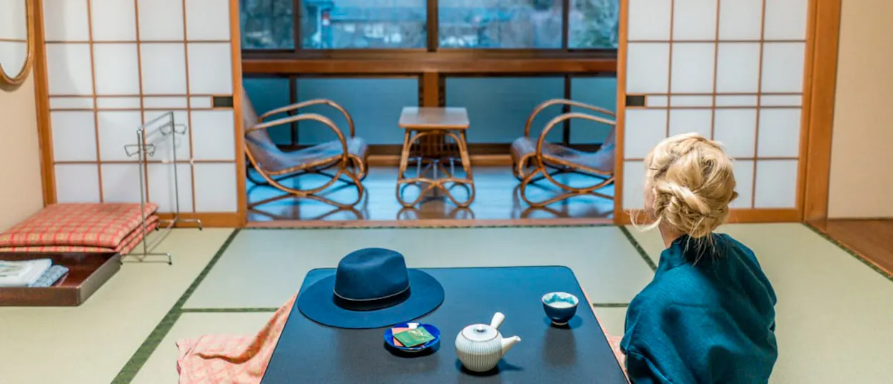 A person sits on tatami mats in a traditional Japanese room, enjoying tea at Koyasan.