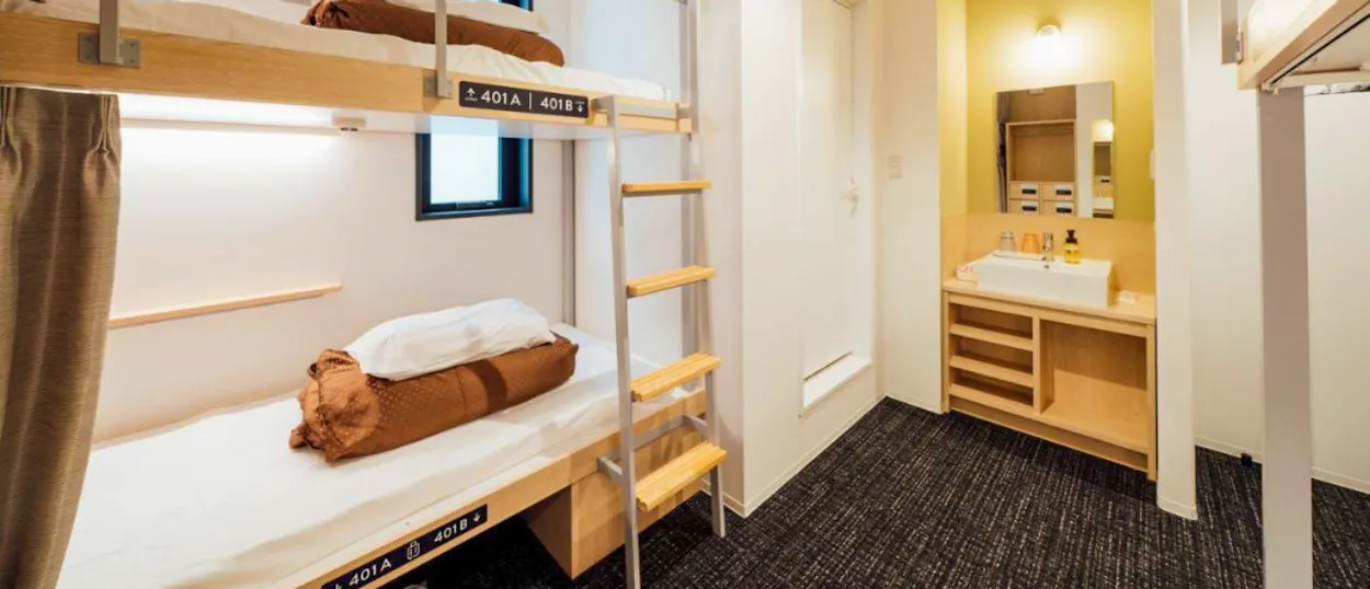 A bright, clean hostel room in Hiroshima with modern bunk beds and a small vanity area.