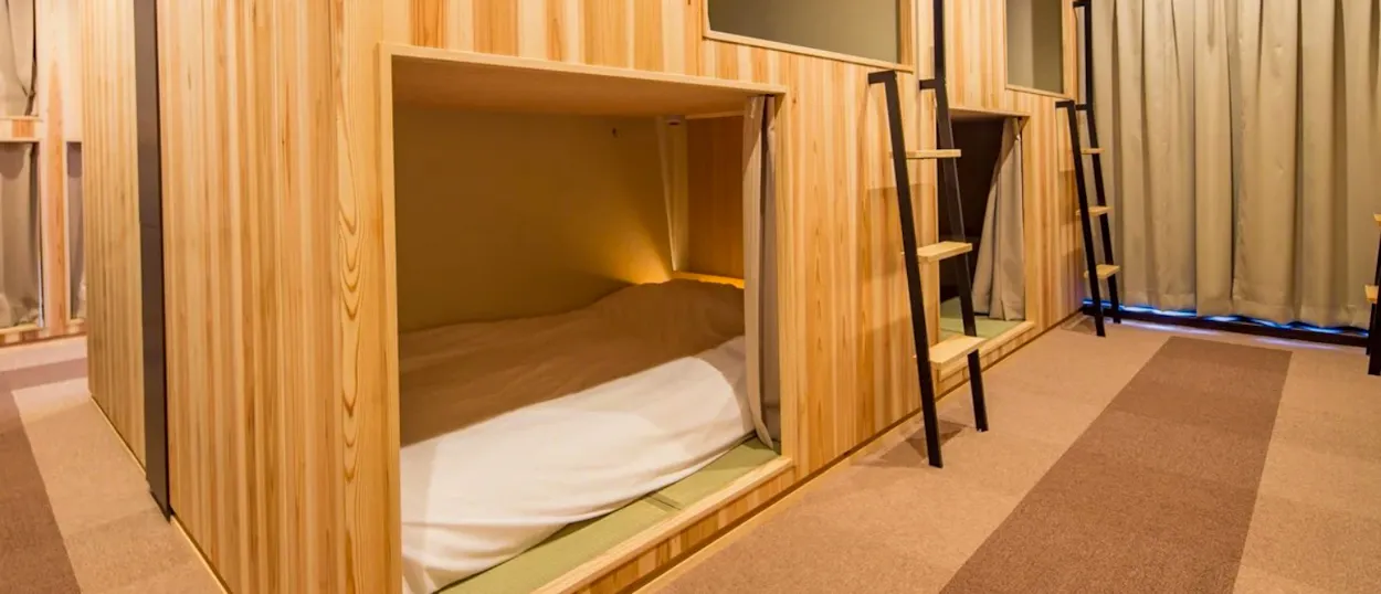 Clean wooden capsule beds with ladders in a modern hostel room in Kyoto, Japan.
