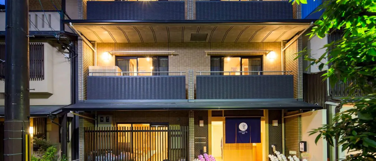 A charming Japanese ryokan hostel in Kyoto's Gion district, warmly lit at dusk.