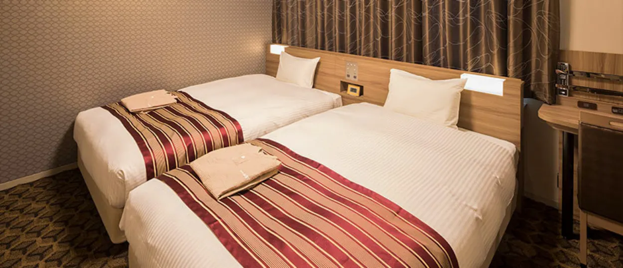 A clean and modern twin hotel room with two beds and striped runners in Osaka.