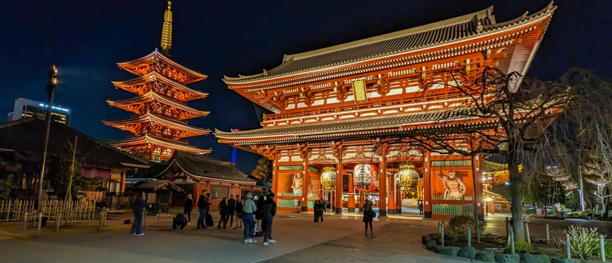Tourists explore the beautifully lit Senso-ji Temple and pagoda in Tokyo at night.