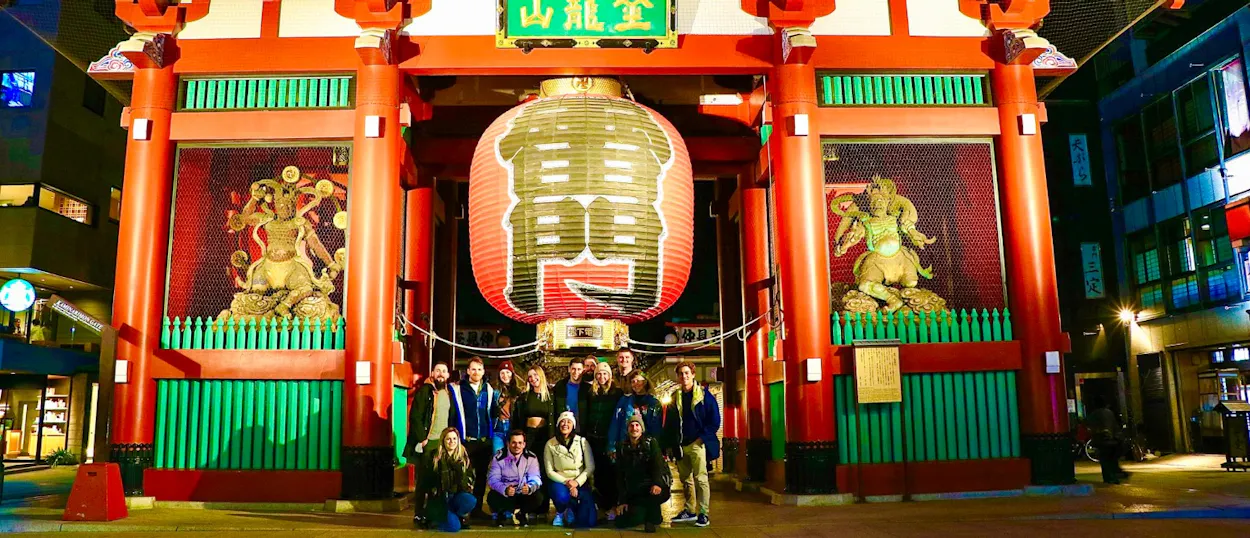 Happy travelers pose before the vibrant, illuminated Kaminarimon gate of Senso-ji Temple in Tokyo.